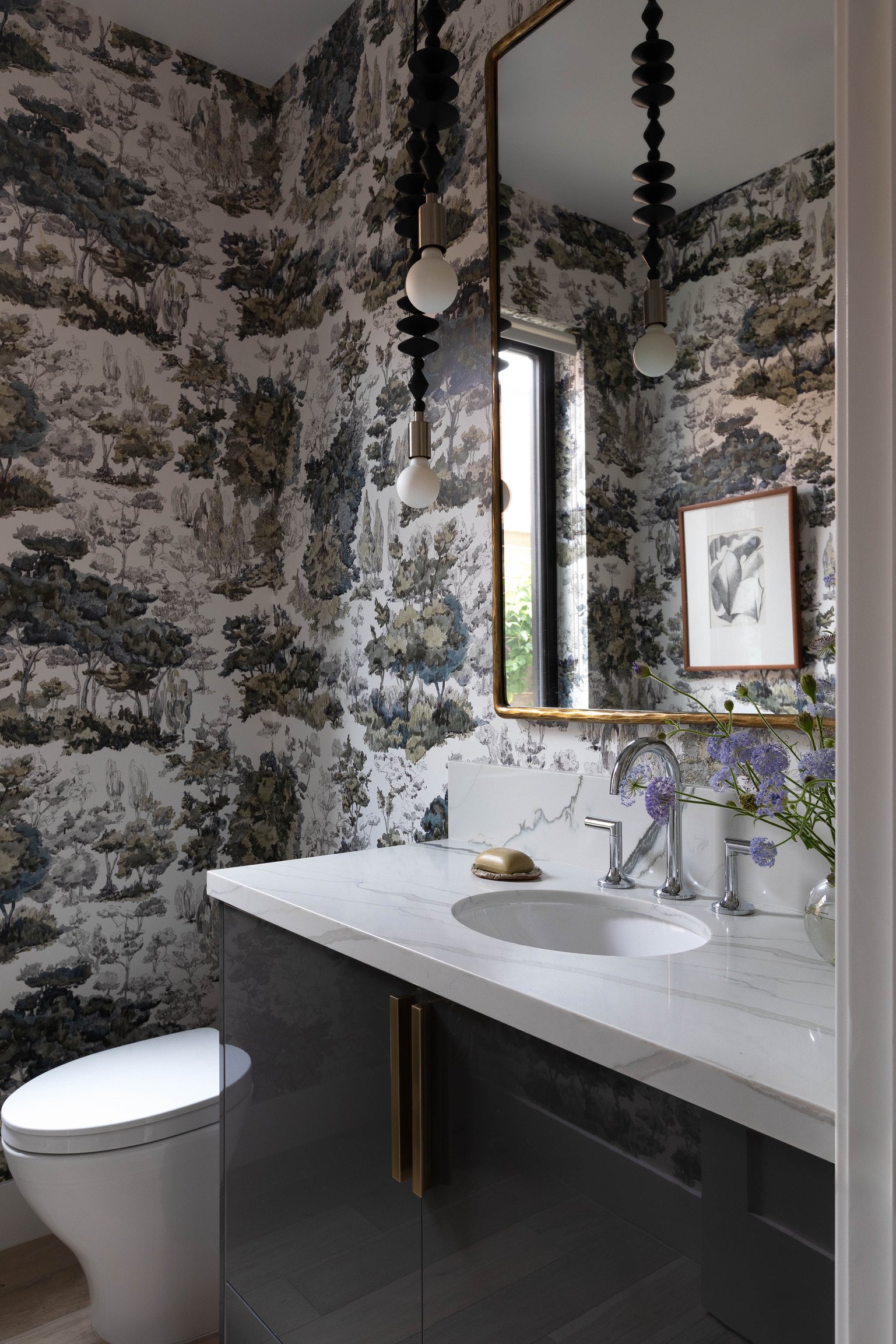 Los Angeles powder bathroom with scenic wallpaper, marble vanity, statement pendant lighting and brass-framed mirror.