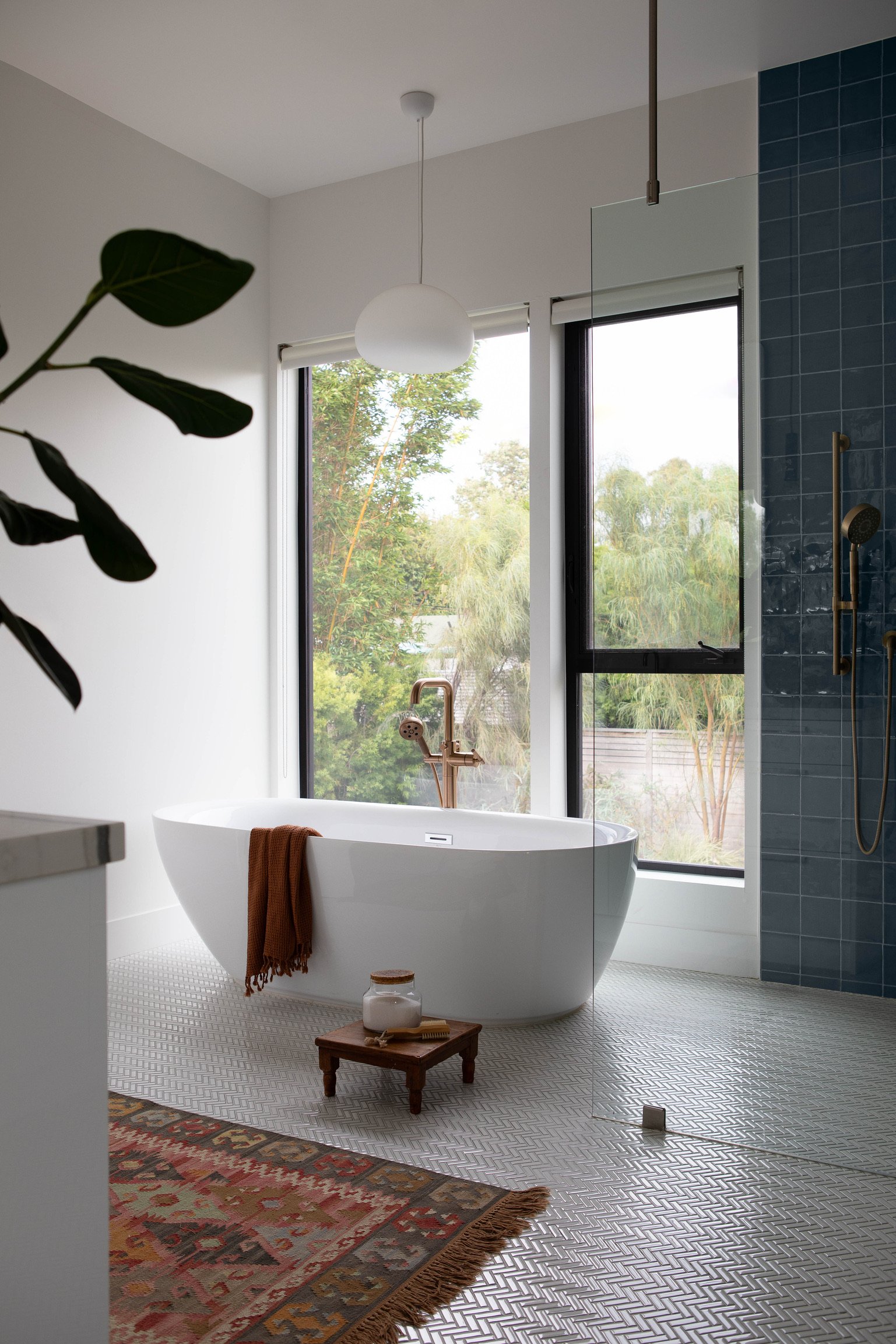 Los Angeles primary bathroom with freestanding soaking tub, blue tile shower, patterned flooring and expansive garden views.