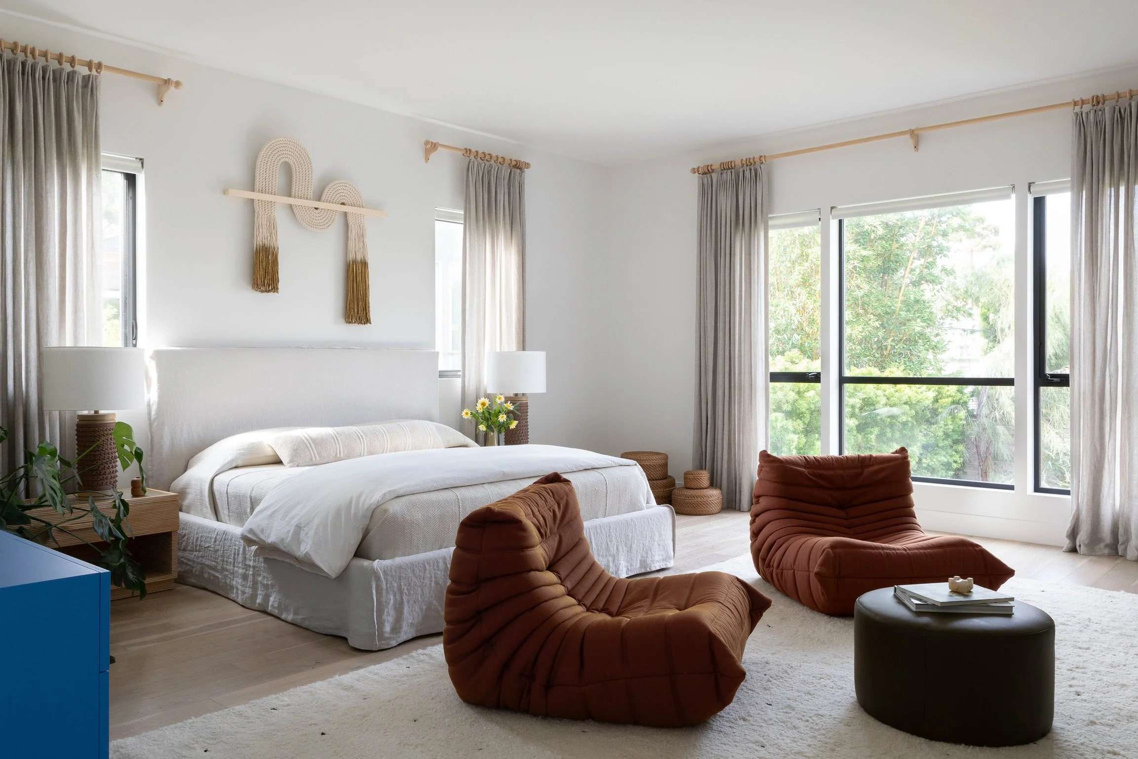 Los Angeles primary bedroom with custom drapery, sculptural lounge chairs, layered natural textures and modern design.