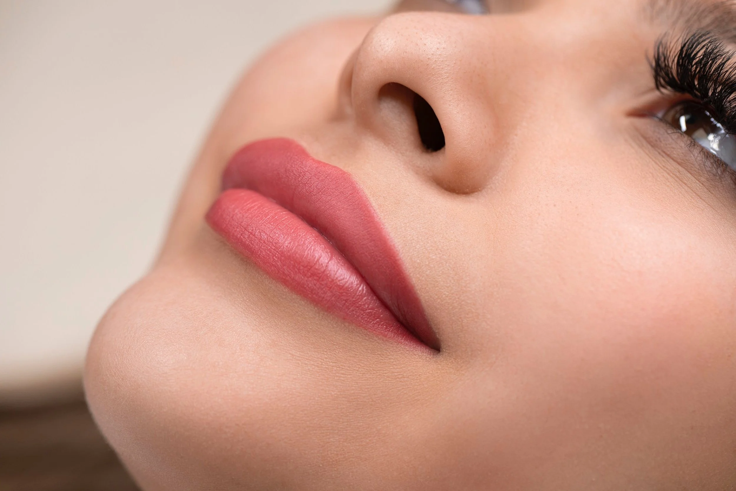 Close-up of a woman's face showing her lips, nose, and one eye with long lashes.