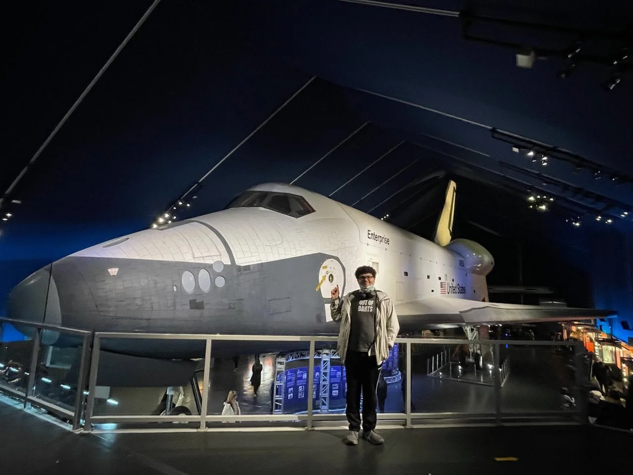 A person standing in front of a real Space Shuttle displayed in a museum.