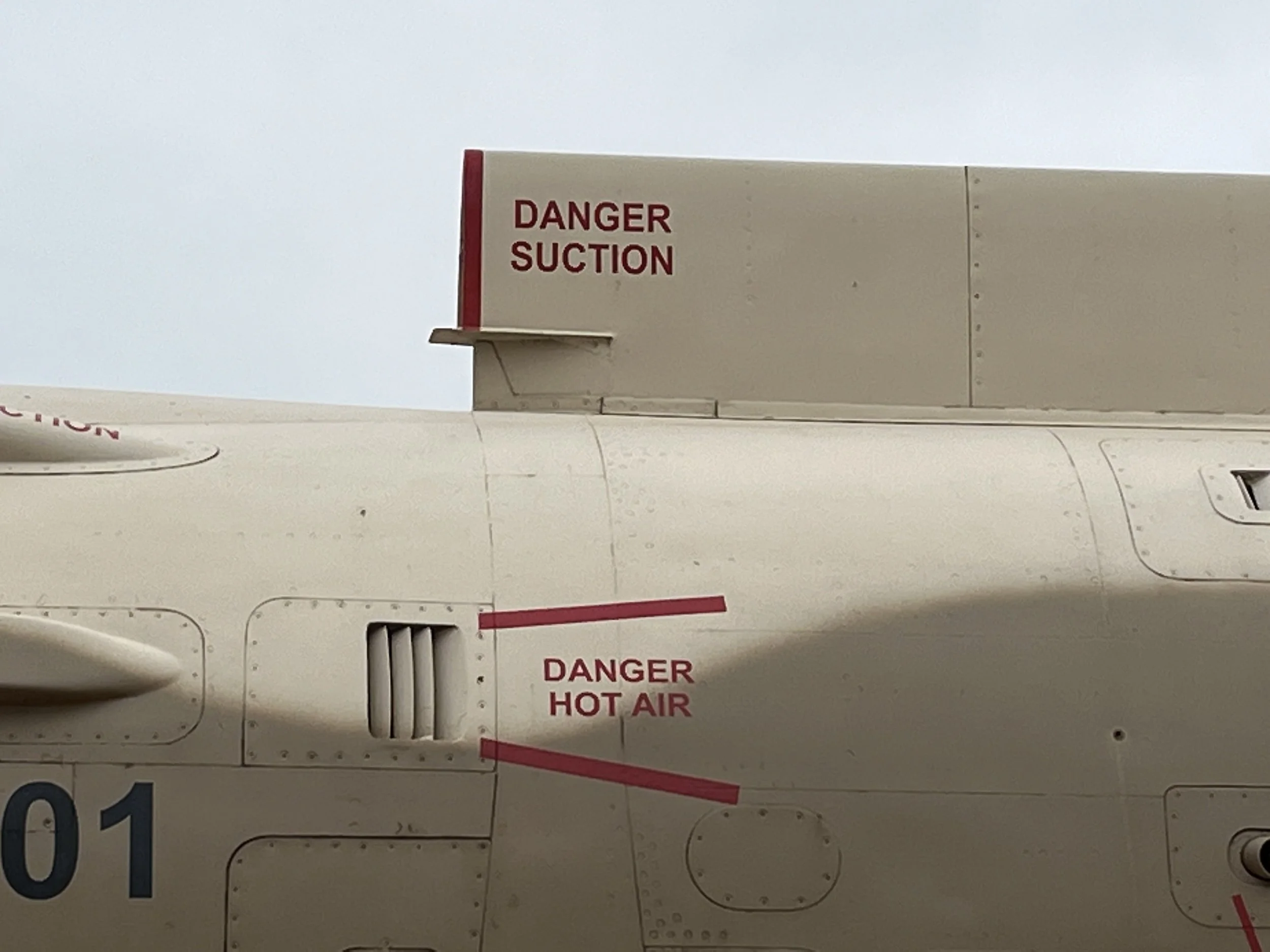 Close-up of an aircraft fuselage with warning labels in red, including 'DANGER SUCTION' and 'DANGER HOT AIR'.