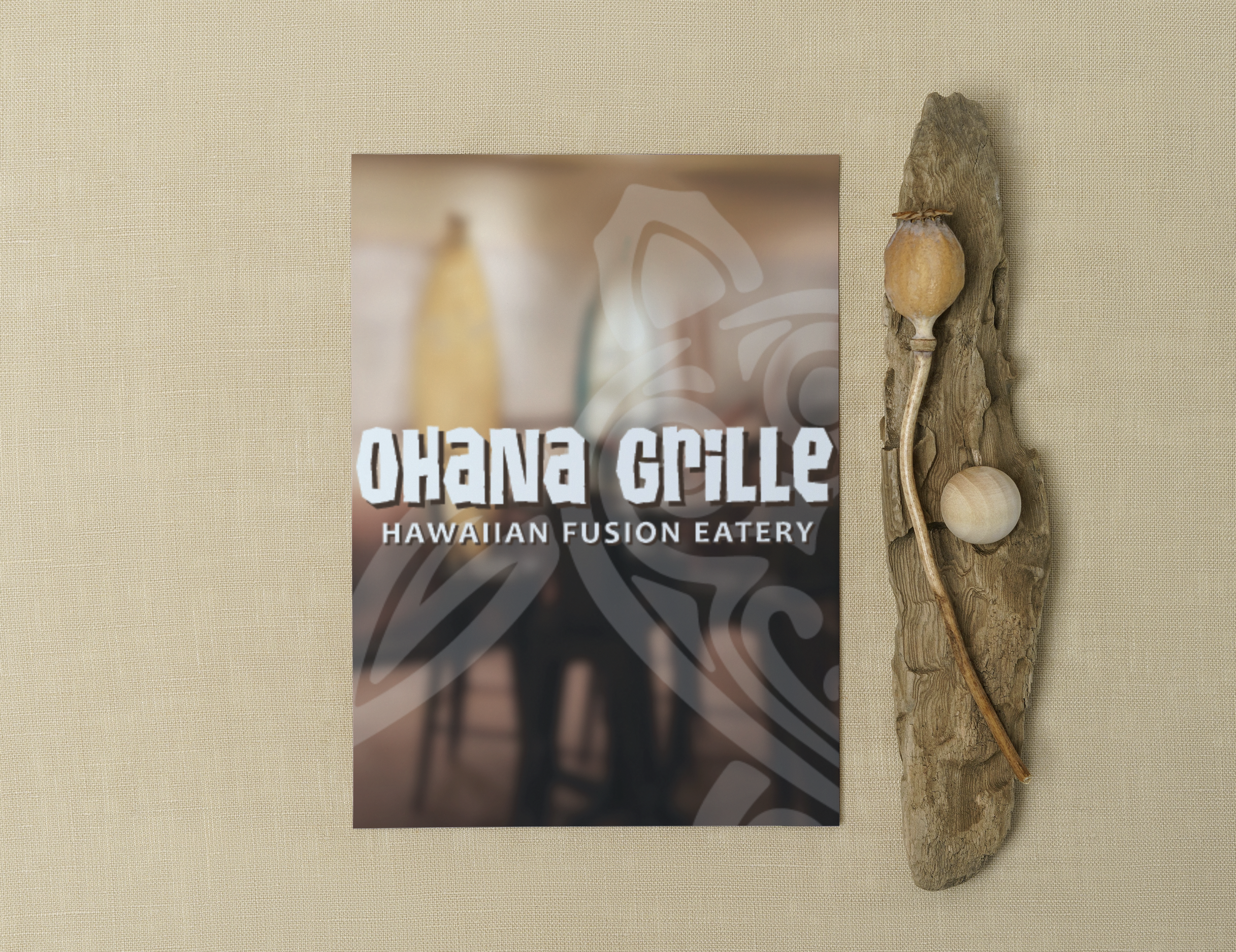 Sign for Ohana Grille, a Hawaiian fusion eatery, on a beige wall with a piece of driftwood art decor featuring a small gourd, a round stone, and a curved branch.