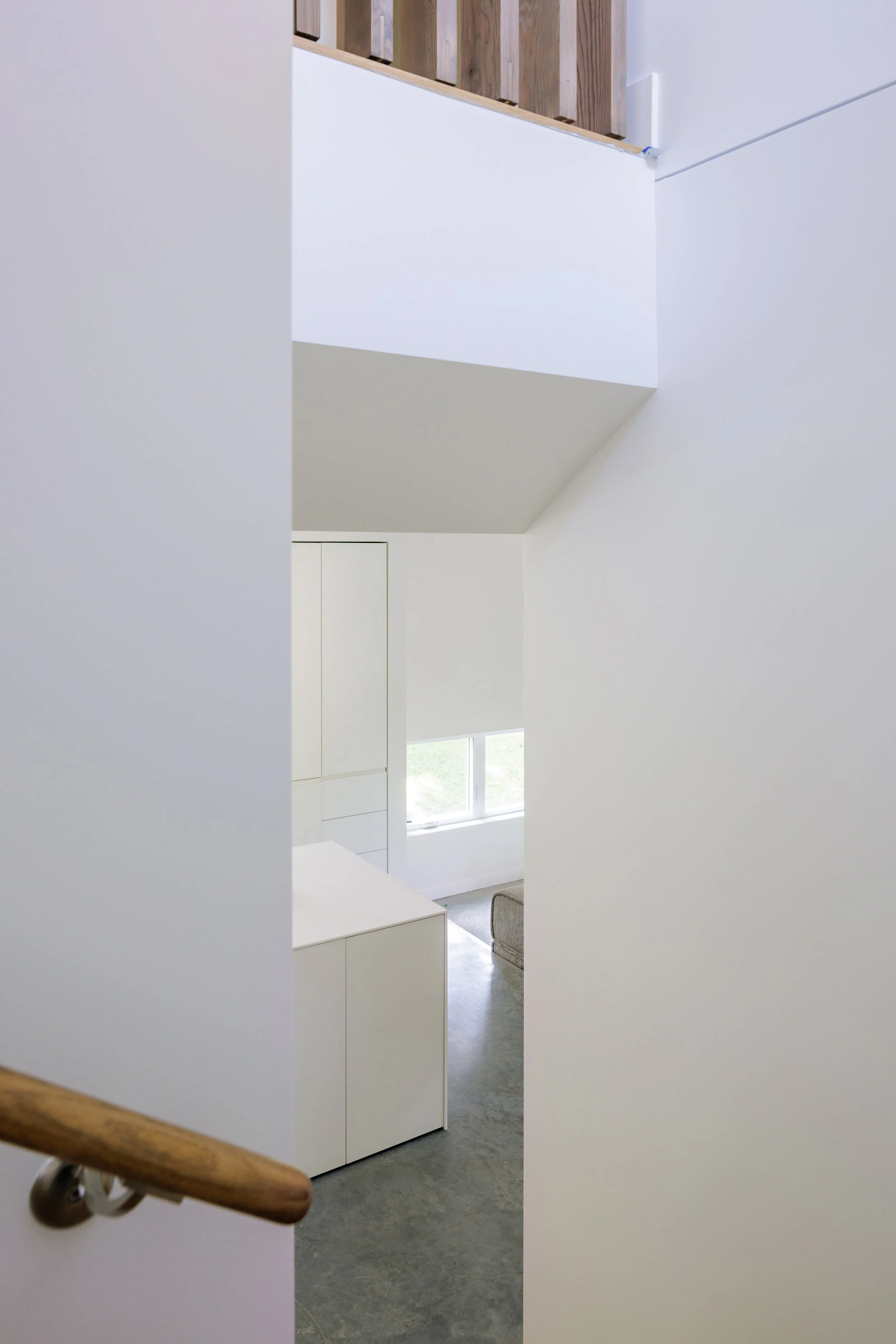 View through a narrow doorway into a bright, modern interior with white walls, a window, and a glimpse of a gray sofa.
