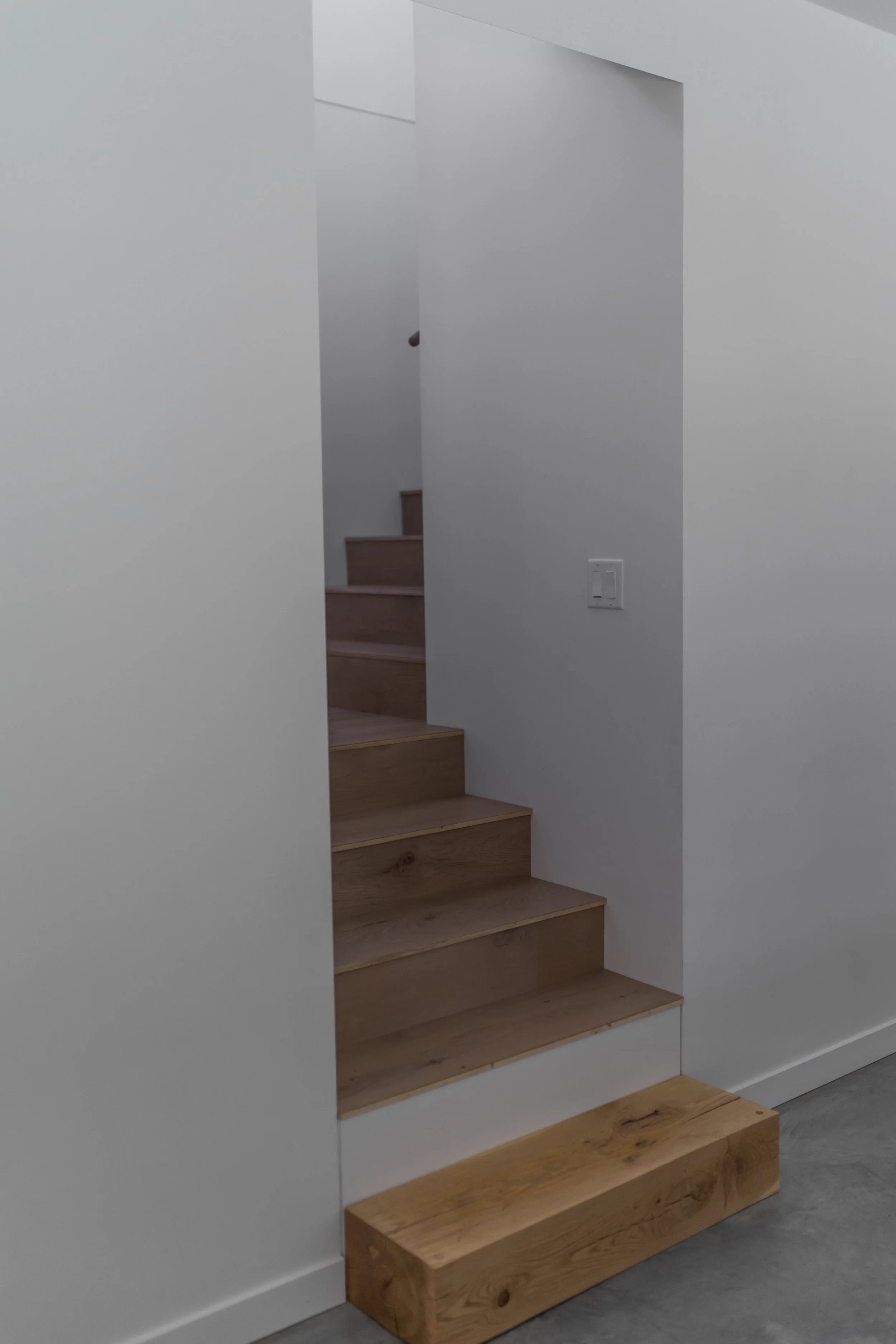Wooden stairs with a white wall on each side, in an interior space.