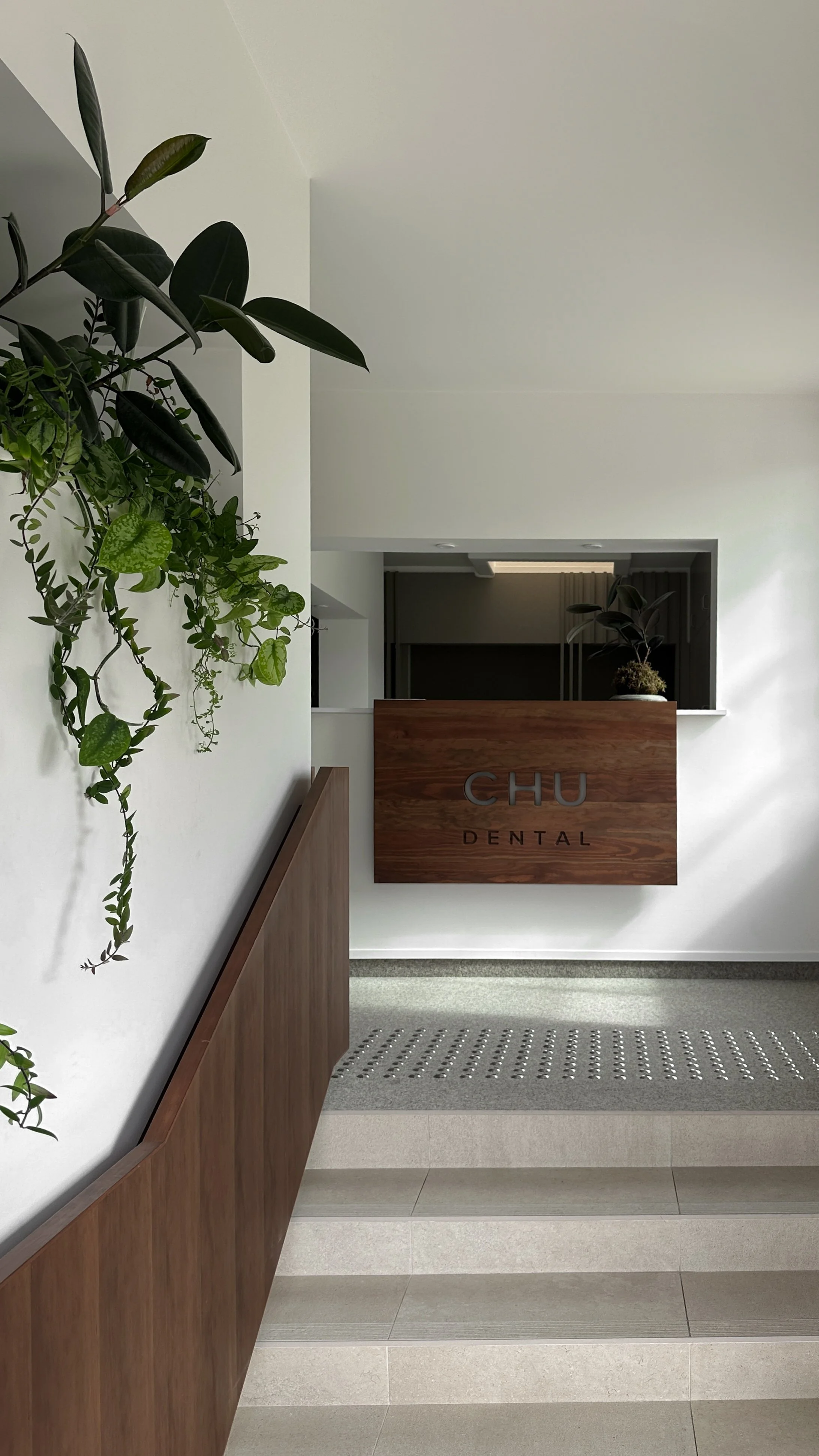Interior view of a dental clinic reception area with a wooden sign reading 'CHU DENTAL,' greenery on the walls, and modern decor.