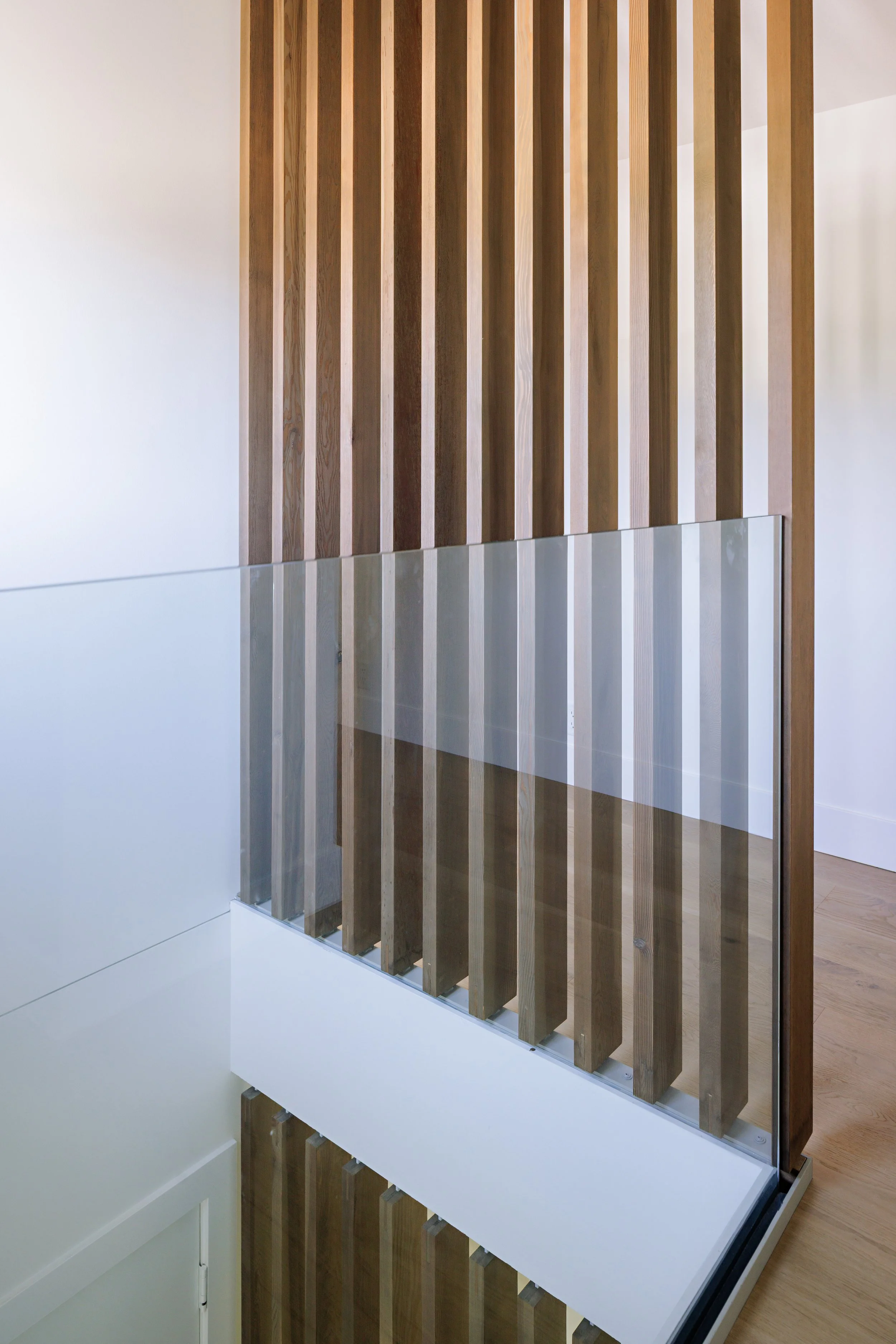 Interior view of a modern wooden slat partition with a glass panel, set inside a minimalist room with white and light wood walls and flooring.