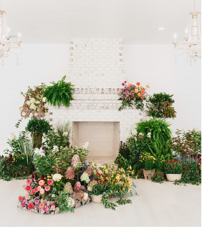 A whitewashed fireplace set up for a wedding ceremony with plants and flowers all around; designed by Fashionable Florist