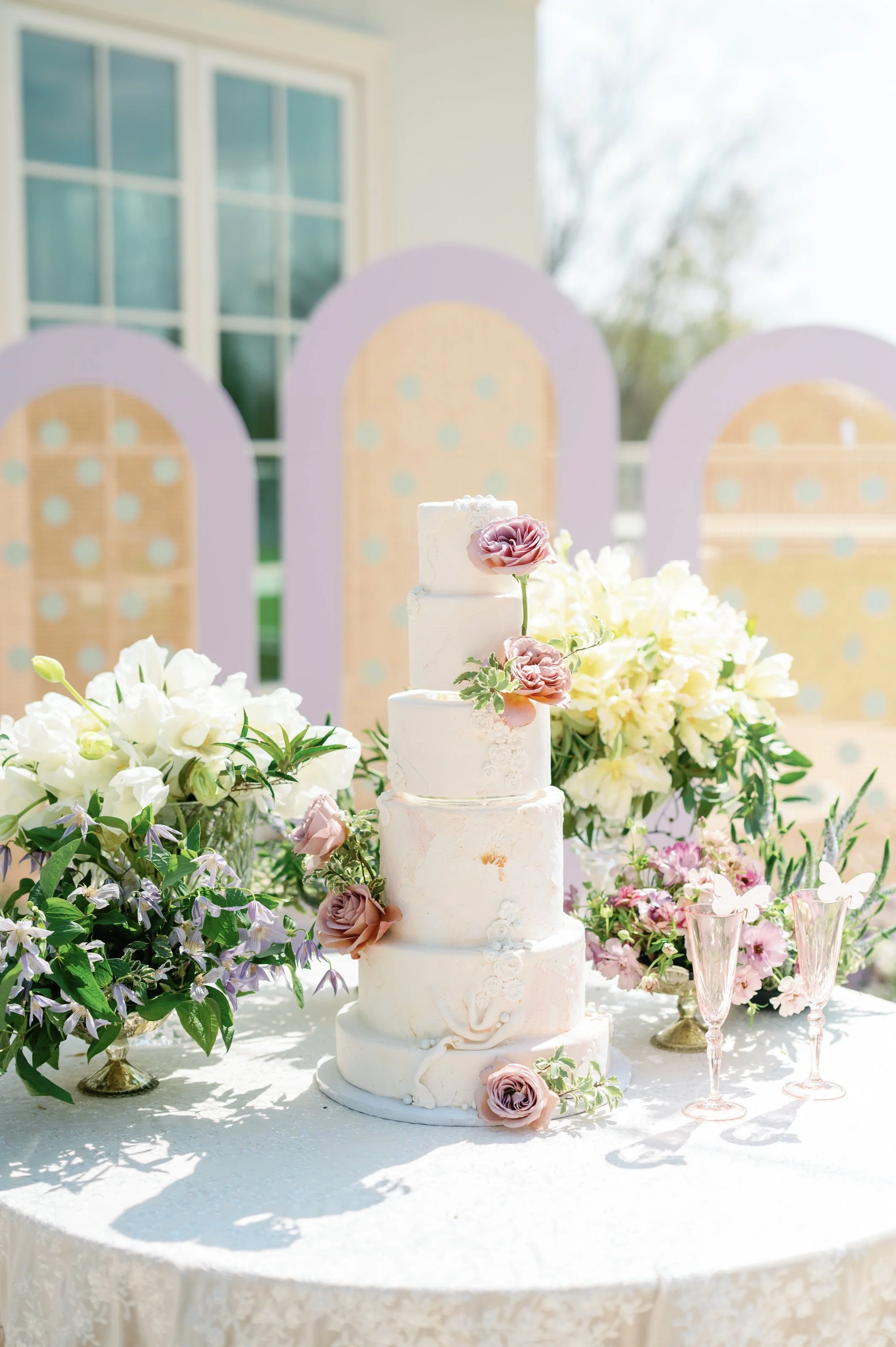 image of a small 4-tier white cake with florals behind it.