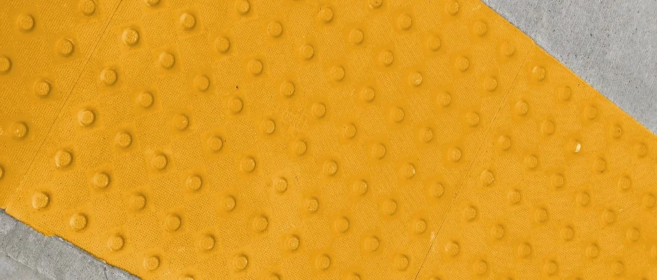 Close-up of GORA 24x24" safety yellow fiberglass tactile plates embedded into concrete.