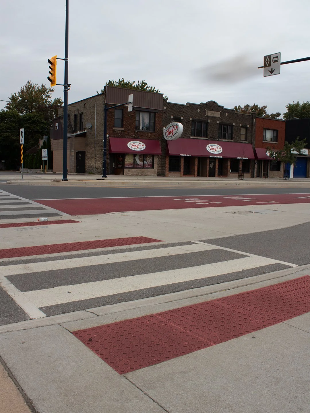 Multi-lane crosswalk with GORA 24x24" brick red steel tactile plates embedded into the concrete just before the intersection that leads up to Tony's in London Ontario.