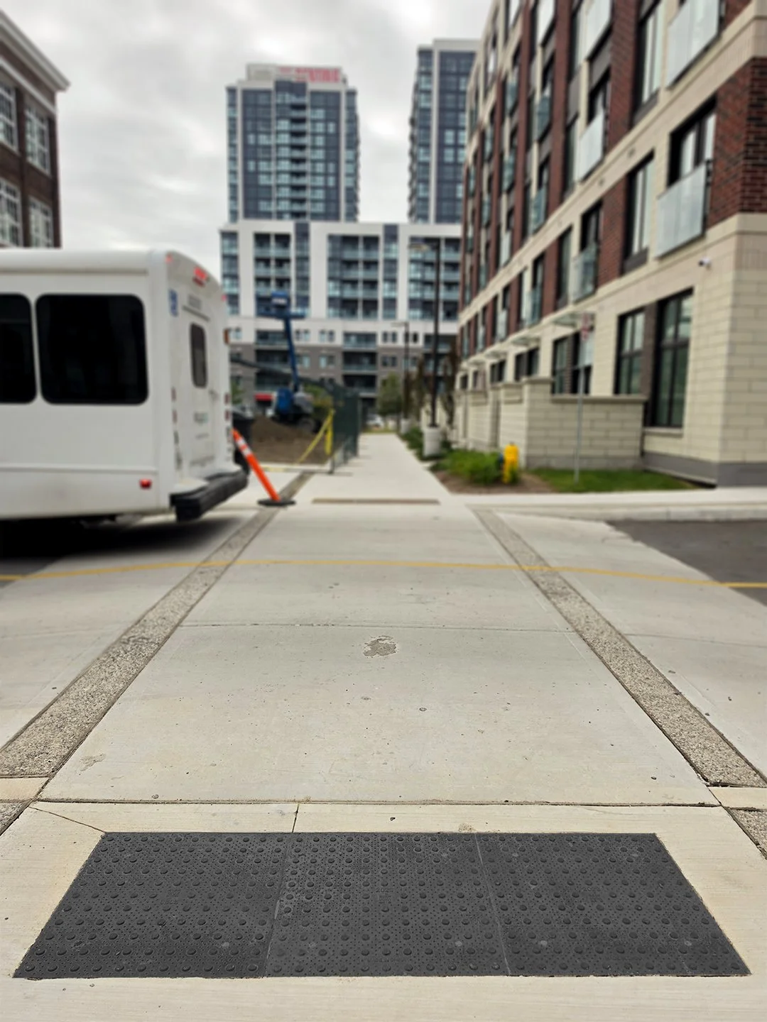 Pedestrian crosswalk in an apartment complex with GORA 24x24" onyx black steel tactile plates just before the intersection, there is construction in the background surrounded by mid-rise and high-rise buildings.