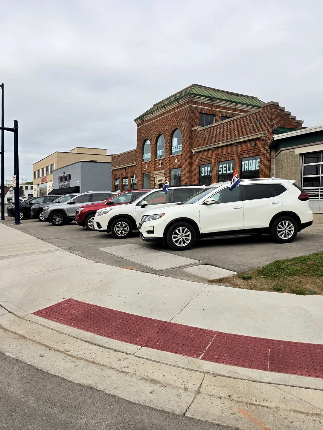 A car dealership on Dundas and Burbrook with GORA brick red steel tactile and radial plates in front of the building's public pedestrian sidewalk crossing.