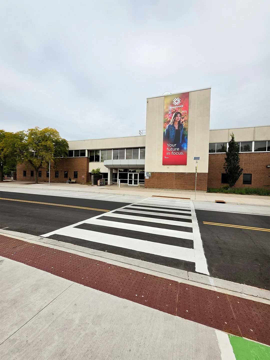 A pedestrian crossing at Fanshawe College London Ontario Main Campus with GORA 24x24" brick red steel tactile plates just before the intersection.
