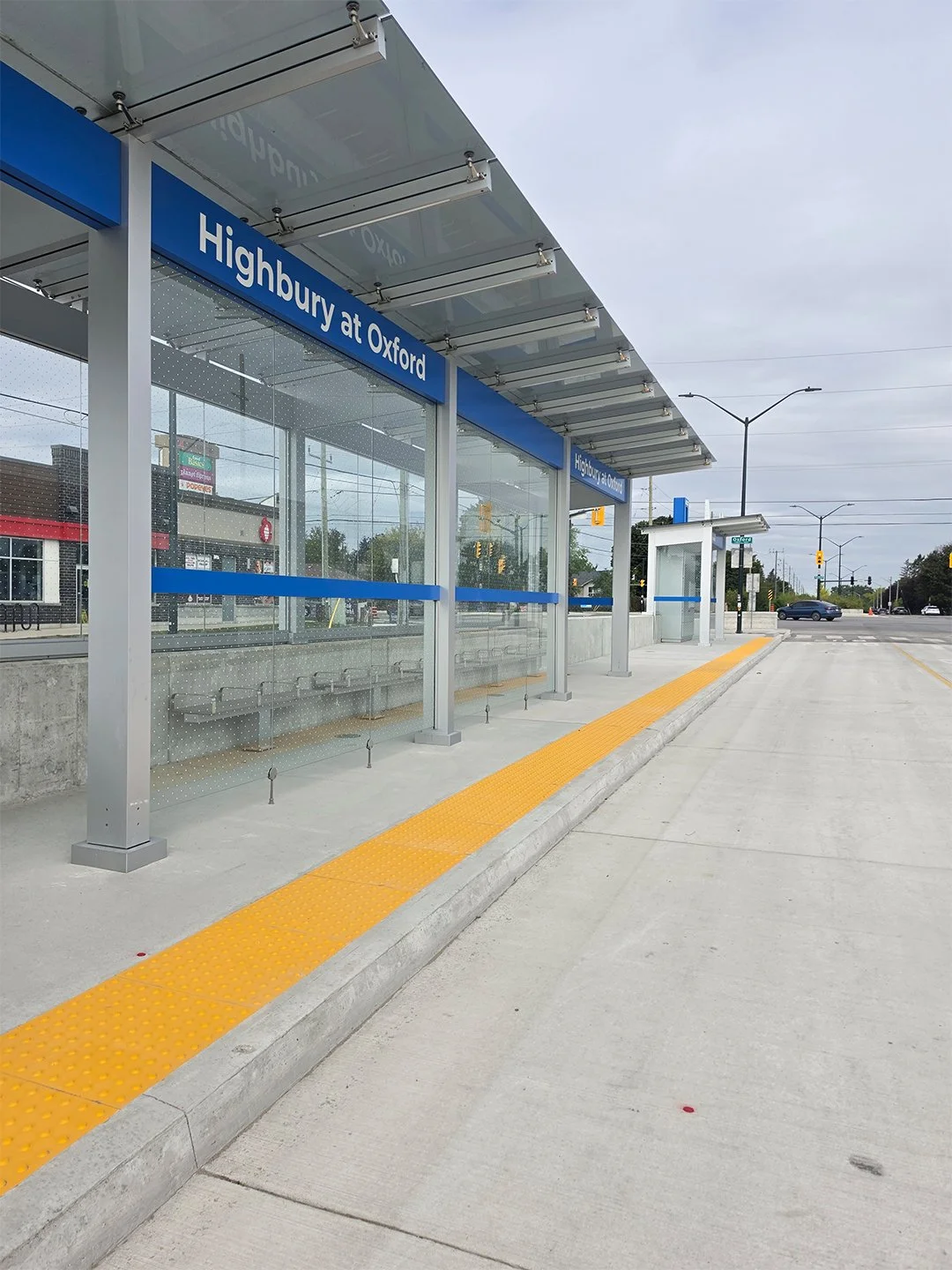 Highbury and Oxford new bus shelter in London Ontario, with GORA 24x24" safety yellow fiberglass tactile plates embedded into the concrete between the bus platform and the road.
