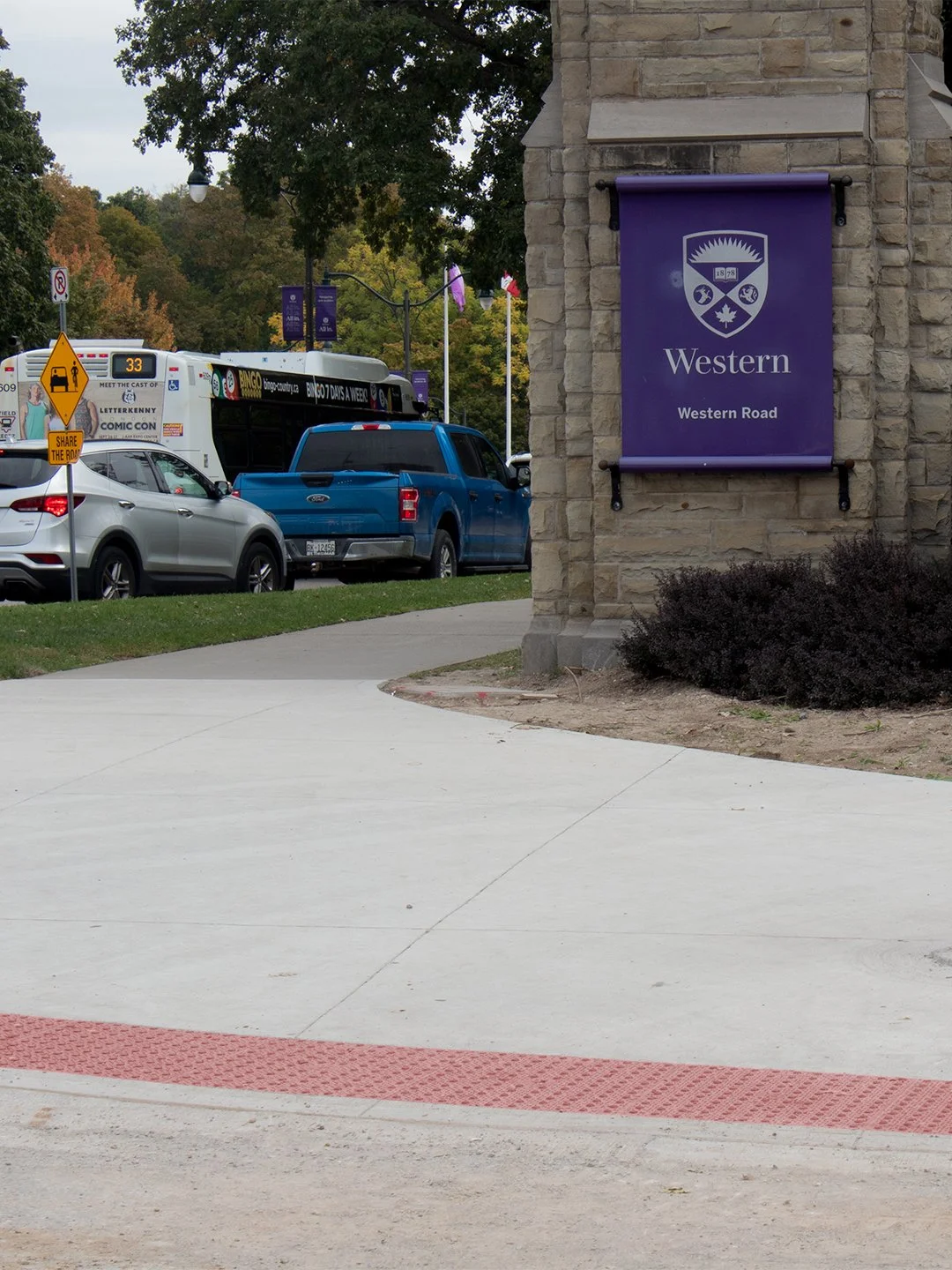 Pedestrian crosswalk leading up to Western University in London Ontario. The sidewalk has GORA brick red steel tactile and radial plates embedded down just before the intersection.