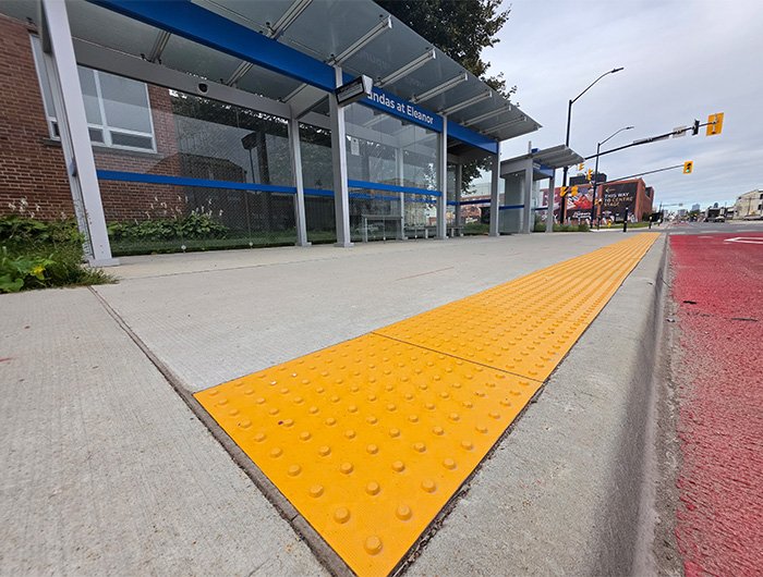Dundas and Eleanor new transit line bus shelter with GORA 24x24" safety yellow fiberglass tactile plates spanning across the sidewalk.