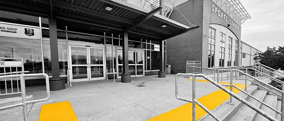 The front entrance of the Western Fair Sports Centre, with GORA removable safety yellow fiberglass tactile plates at the top of the concrete stairway leading up to the centre.