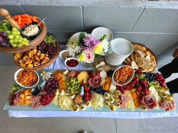 Table with cheese, fruits, vegetables, flowers, and snacks for a buffet or party.