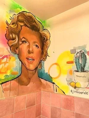 Watercolor-style painting of a woman with wavy, shoulder-length hair, standing against a colorful abstract background. Part of the image shows a tiled wall and a shelf with a vase and lemons.