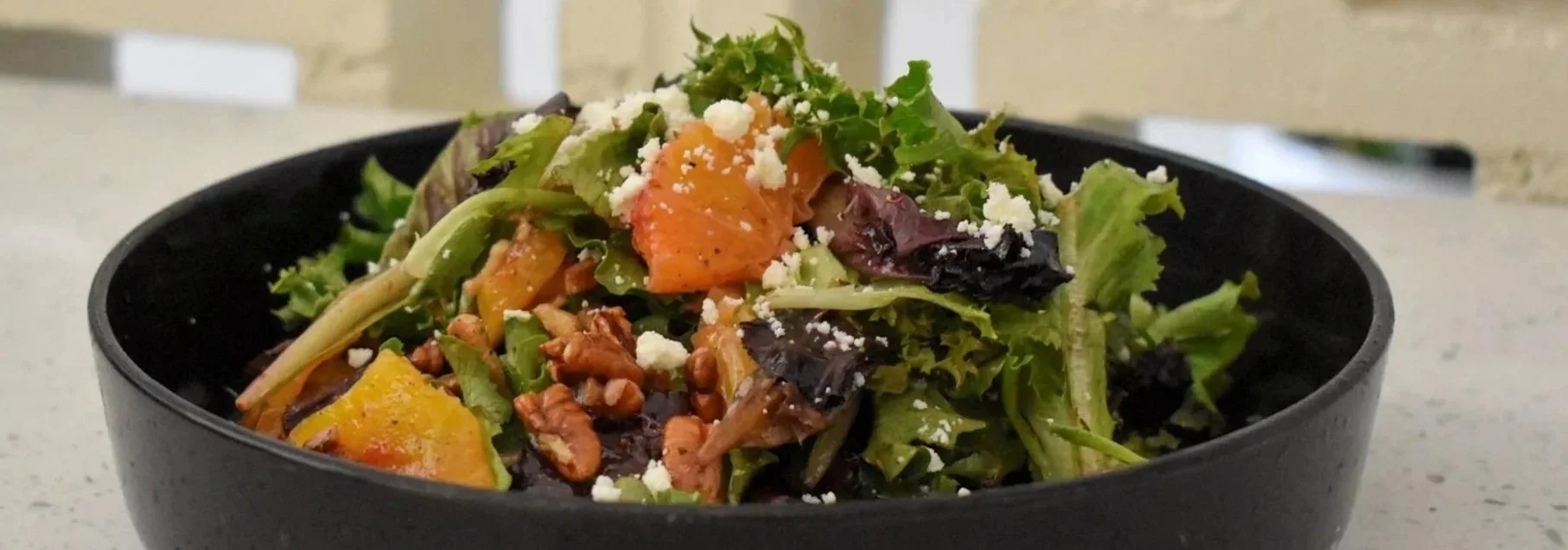 Mixed salad with greens, roasted butternut squash, crumbled cheese, and chopped nuts in a black bowl