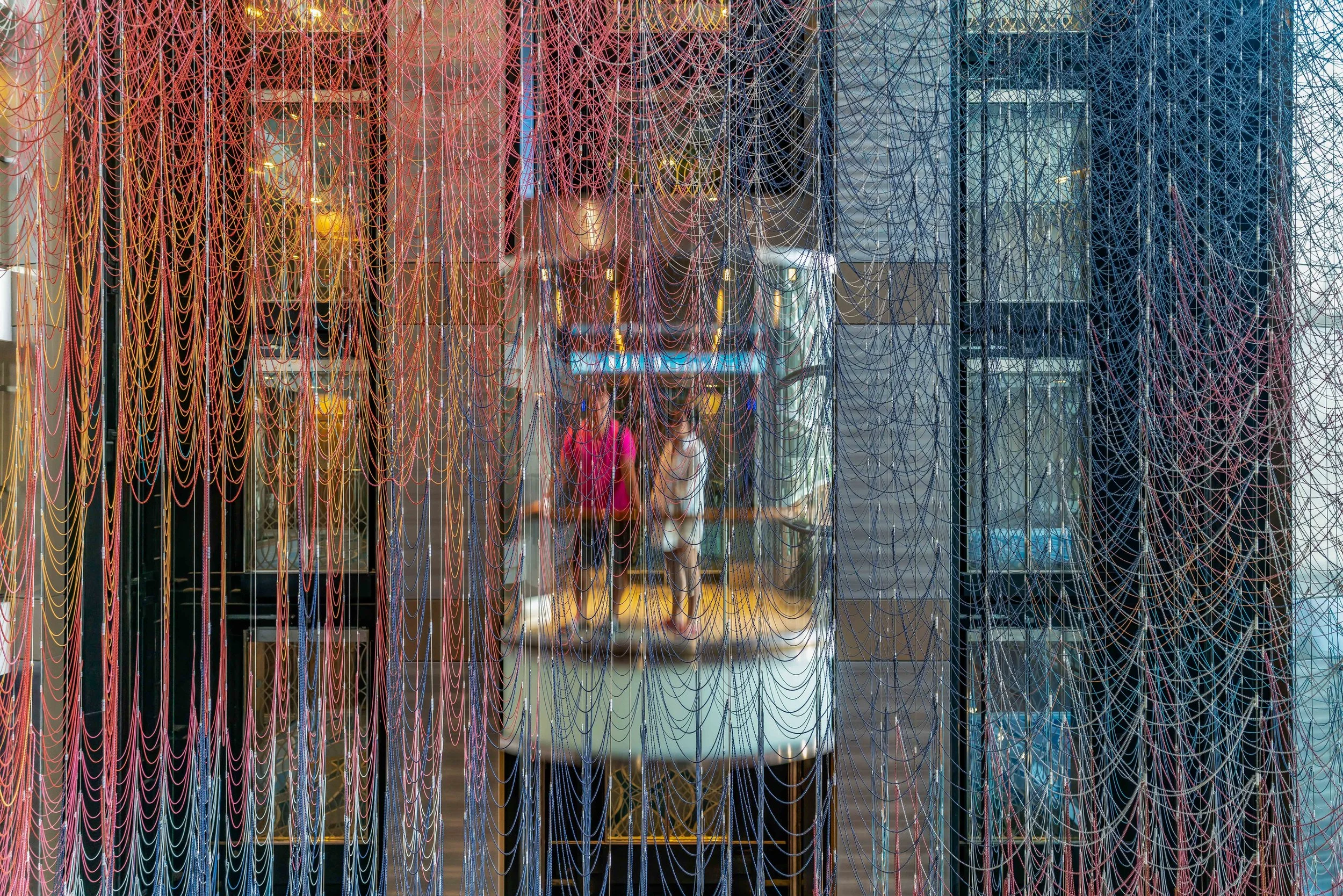 Colorful web-like installation made of strings in red, orange, yellow, blue, and purple covering the glass storefront of a building.