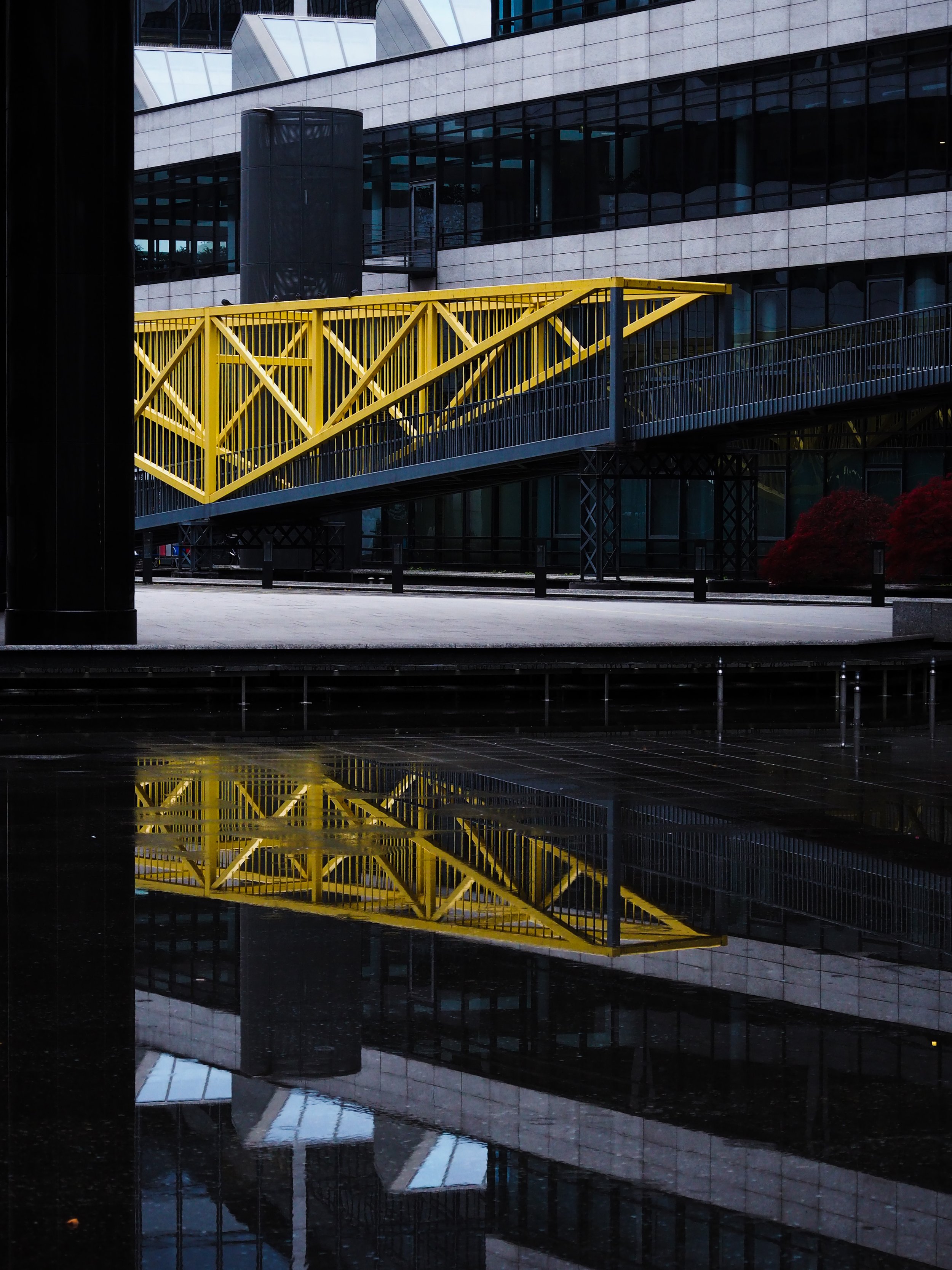 Yellow pedestrian bridge with modern building background and reflection on water surface.