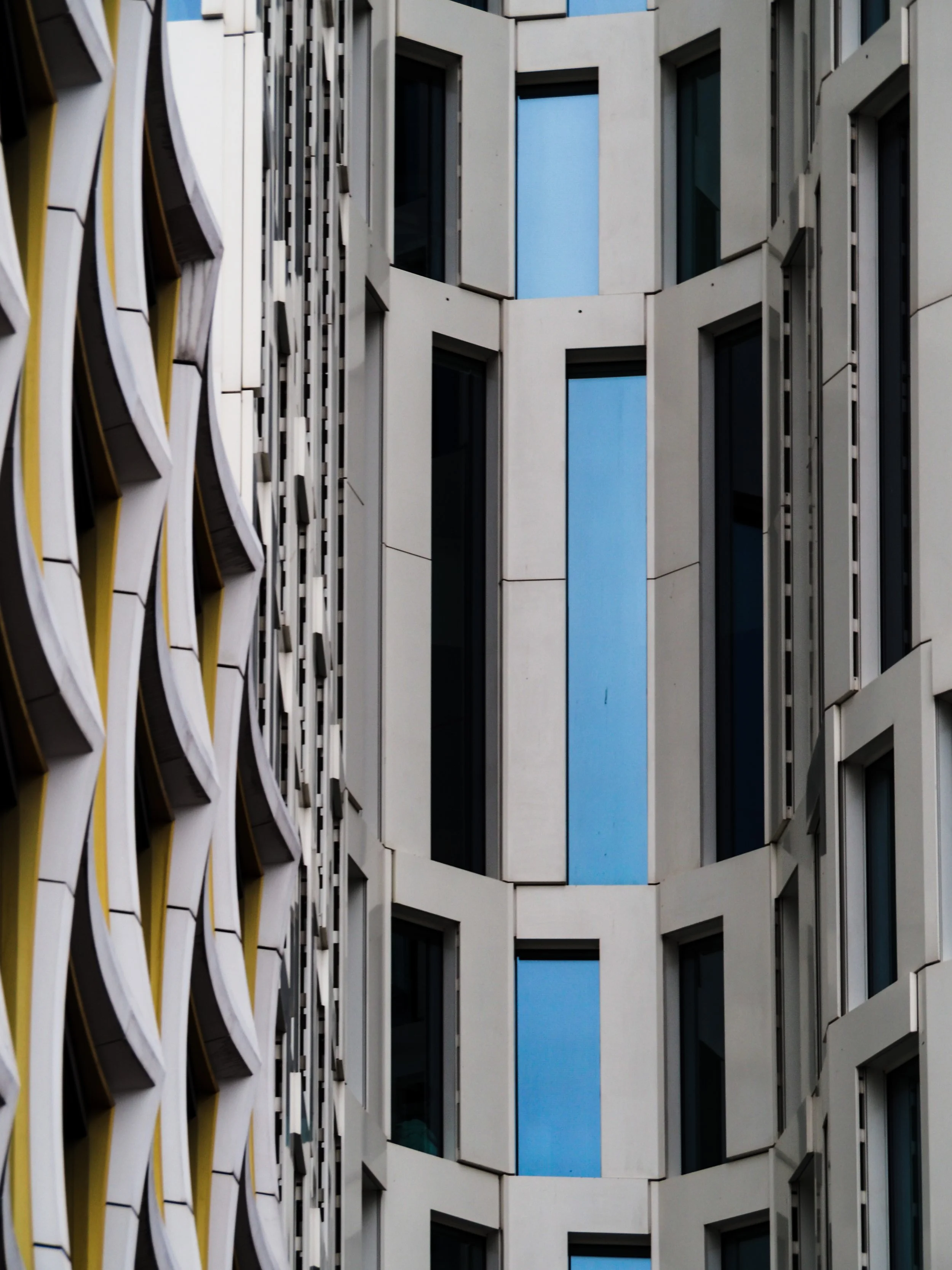 Close-up of modern building exteriors with geometric patterns, featuring blue-tinted glass windows and textured facades.