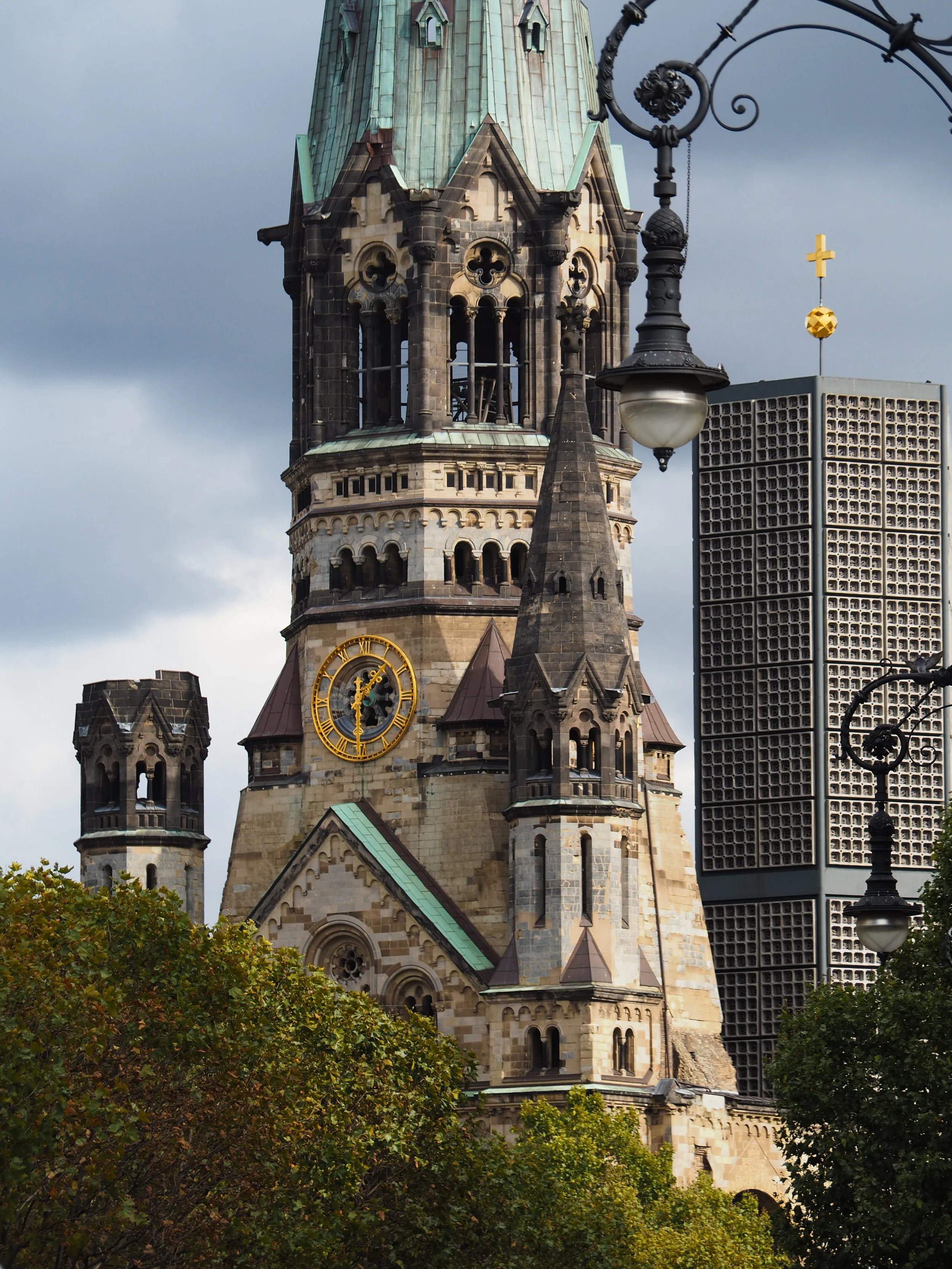 Kaiser Wilhelm Memorial Church in Berlin, Germany, with clock, spire, and modern tower in the background.