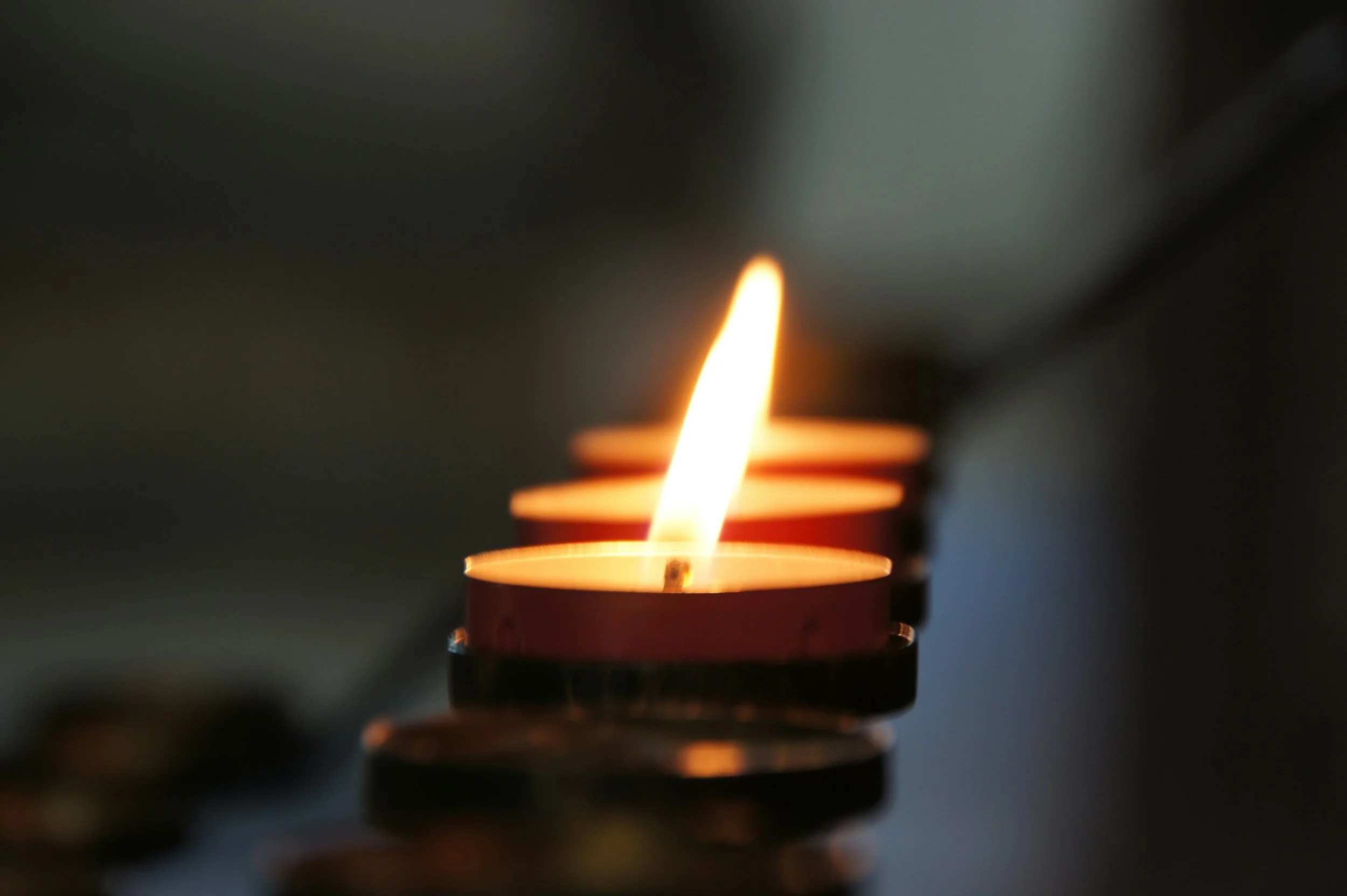 Close-up of a row of tea light candles, with one lit flame burning brightly.
