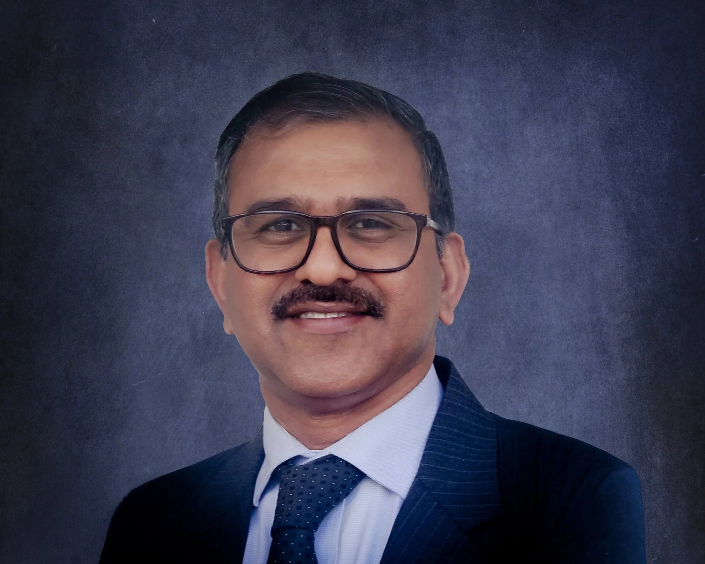 Portrait of a smiling man wearing glasses and a clerical collar, with a blue textured background.