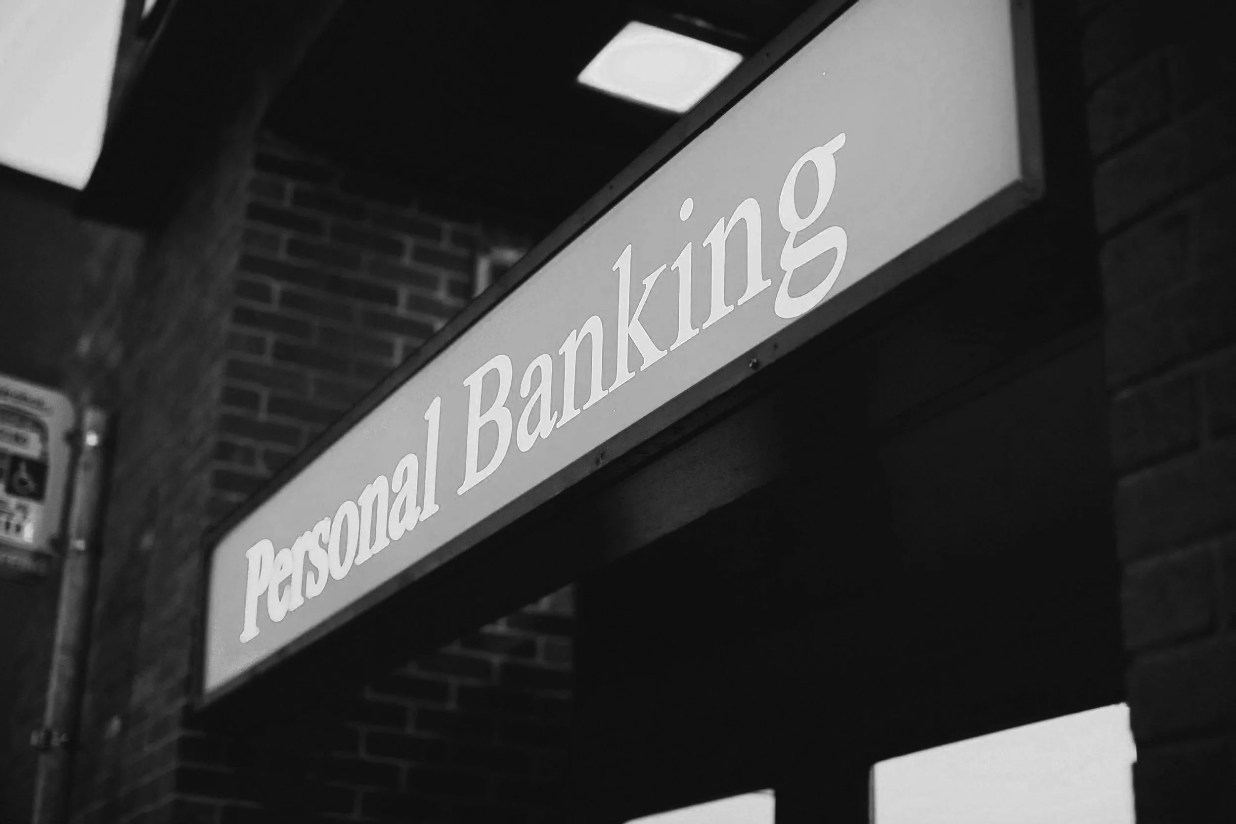 Close-up of a street sign reading 'Personal Banking' attached to a brick building under a dark sky.