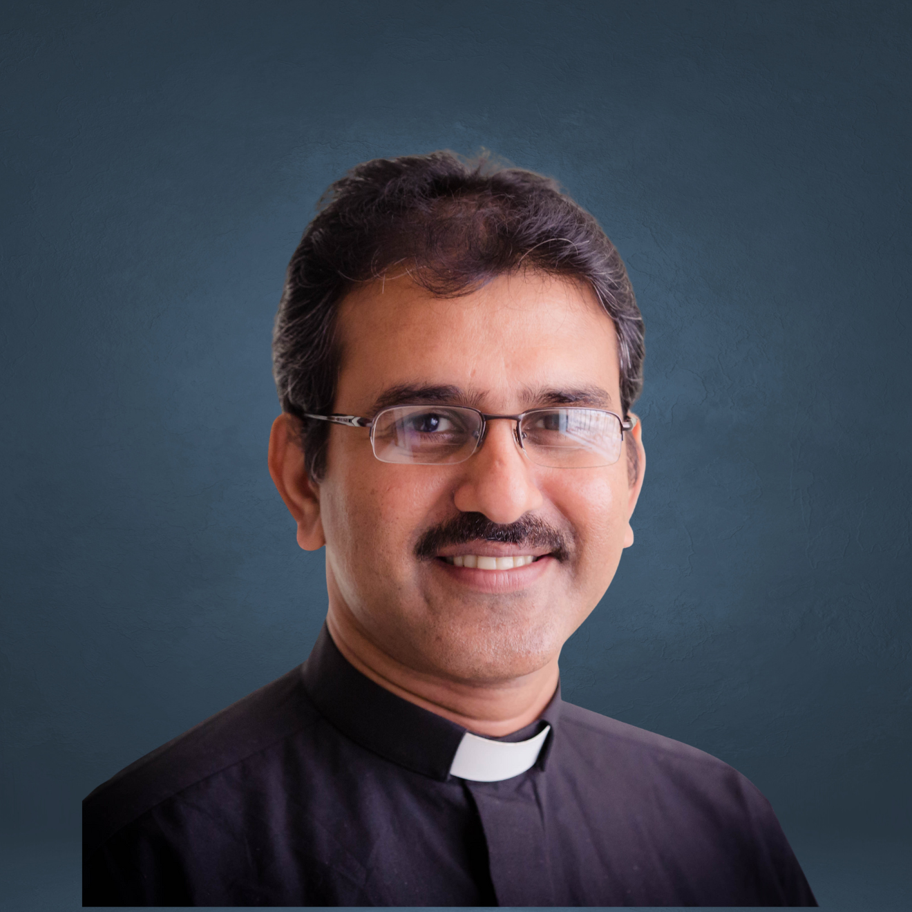Portrait of a smiling man wearing glasses and a clerical collar, with a blue textured background.
