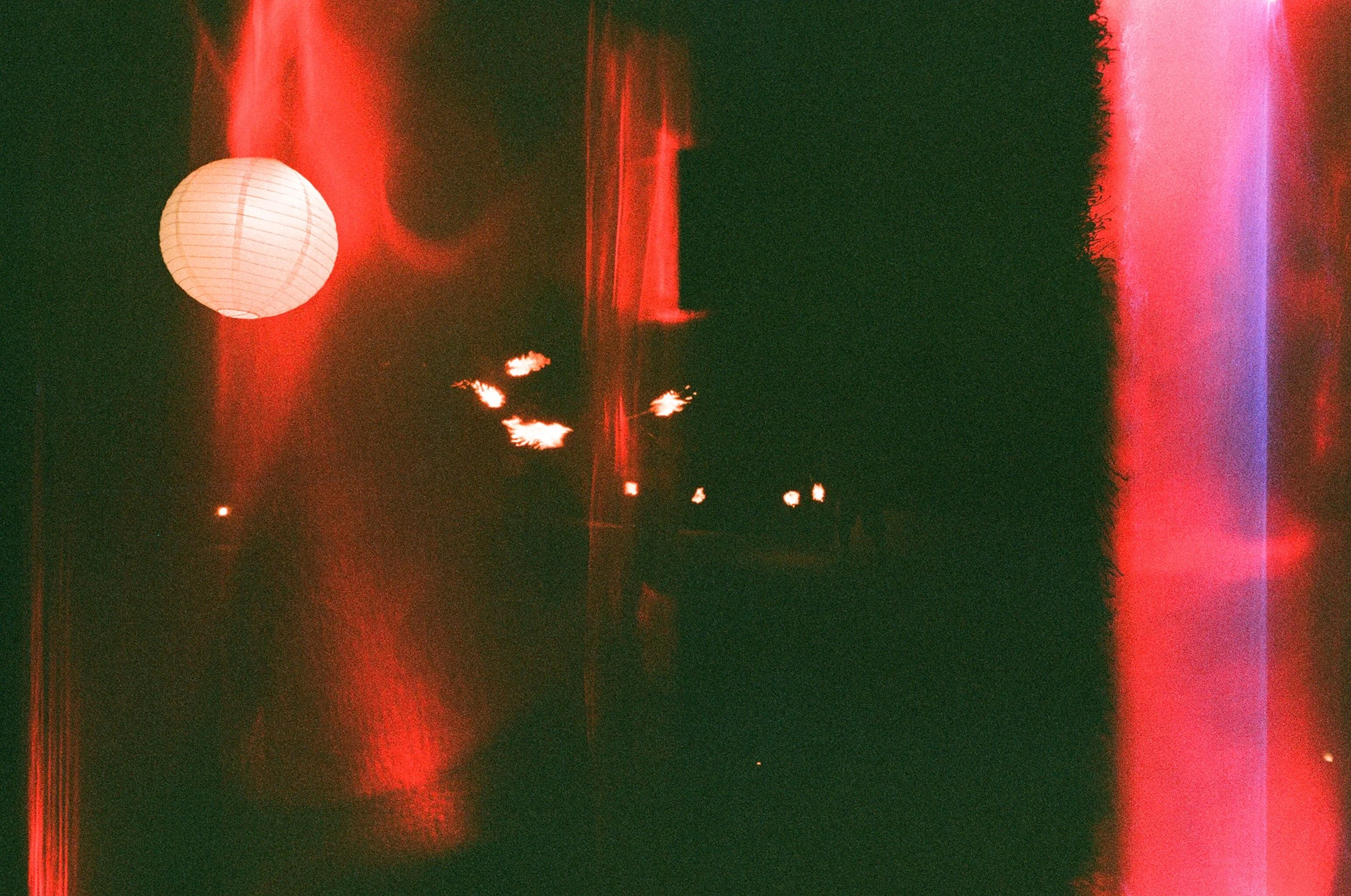 Night scene with glowing paper lantern and bright lights, edited with red and purple color distortion.