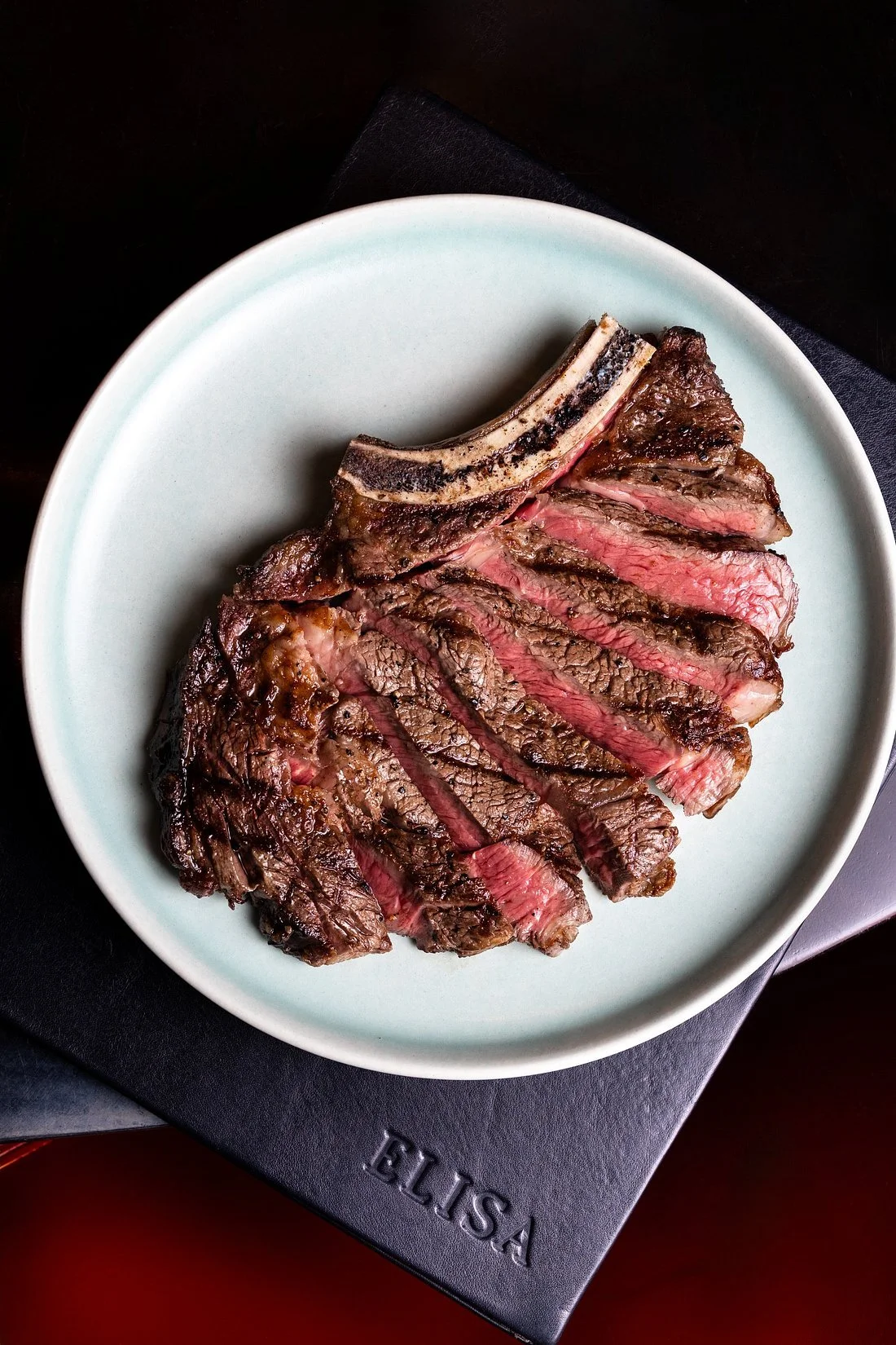A sliced, cooked steak on a white plate, showing a pink center, placed on a black surface.