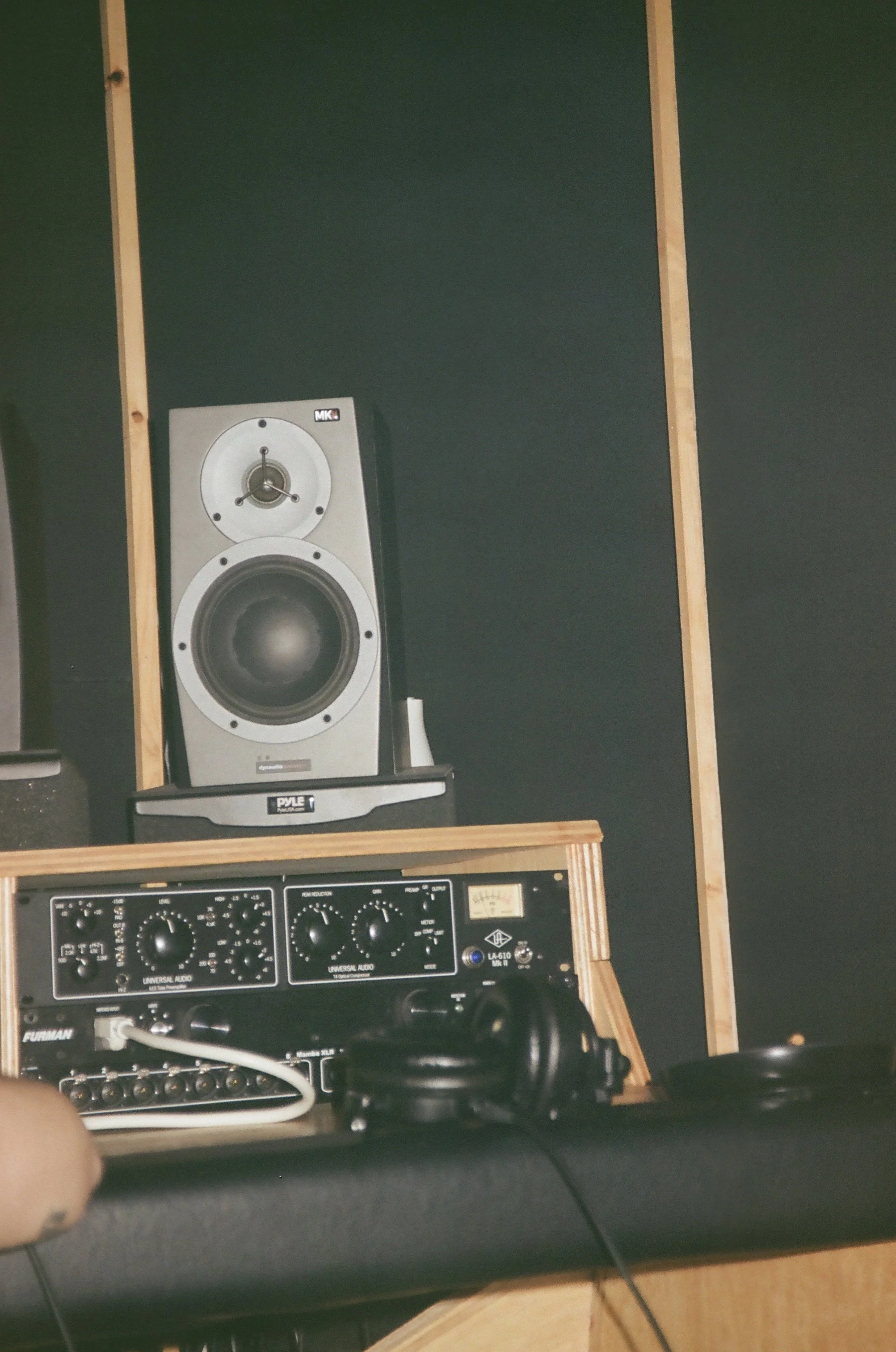 Recording studio with a large monitor speaker on a wooden shelf, audio equipment, headphones, and a black soundproof wall.