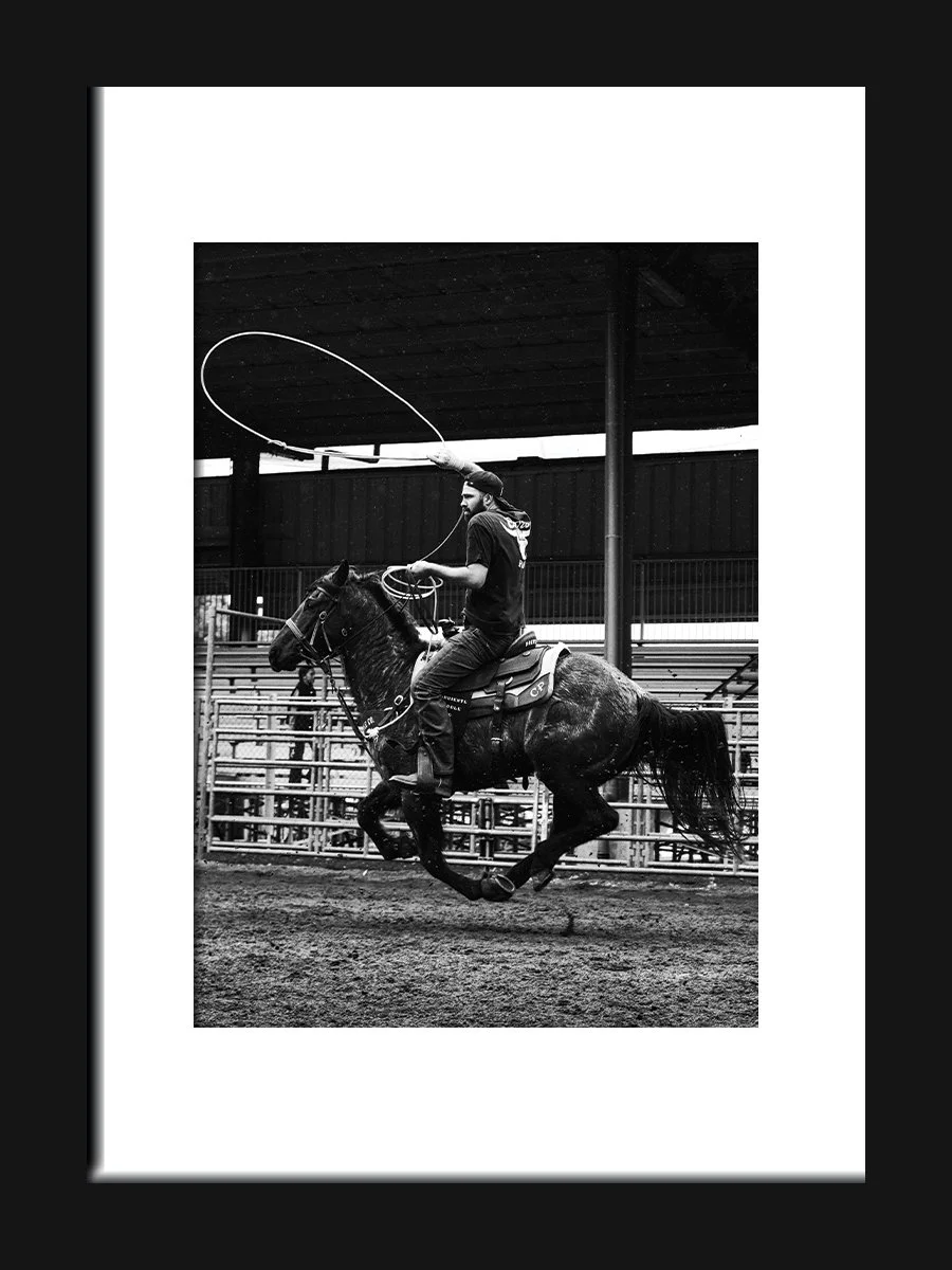 A man riding a horse on an arena, using a lasso in a rodeo event, black and white photo.