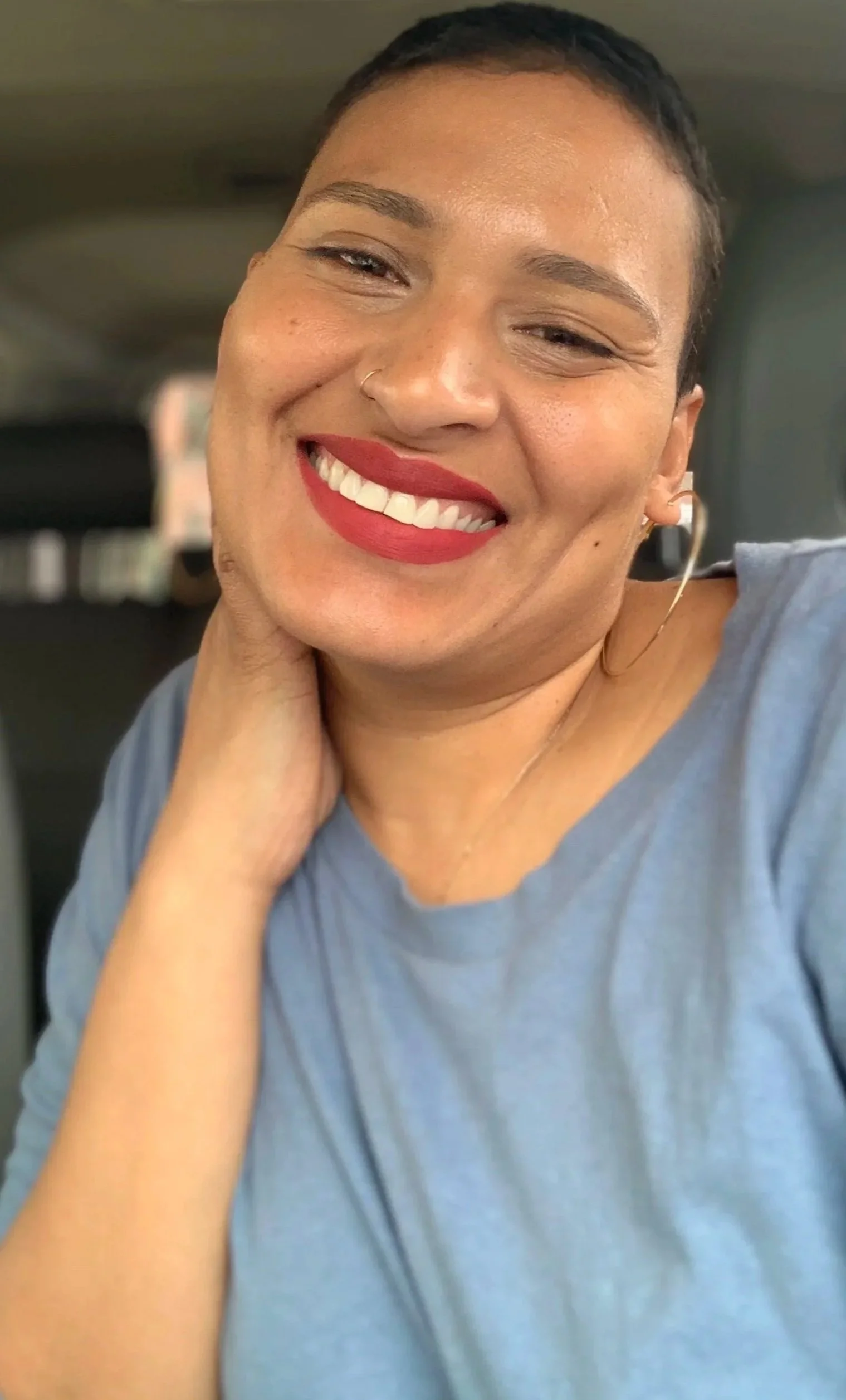 Close-up of a smiling woman with blonde hair, blue eyes, red lipstick, and earrings.