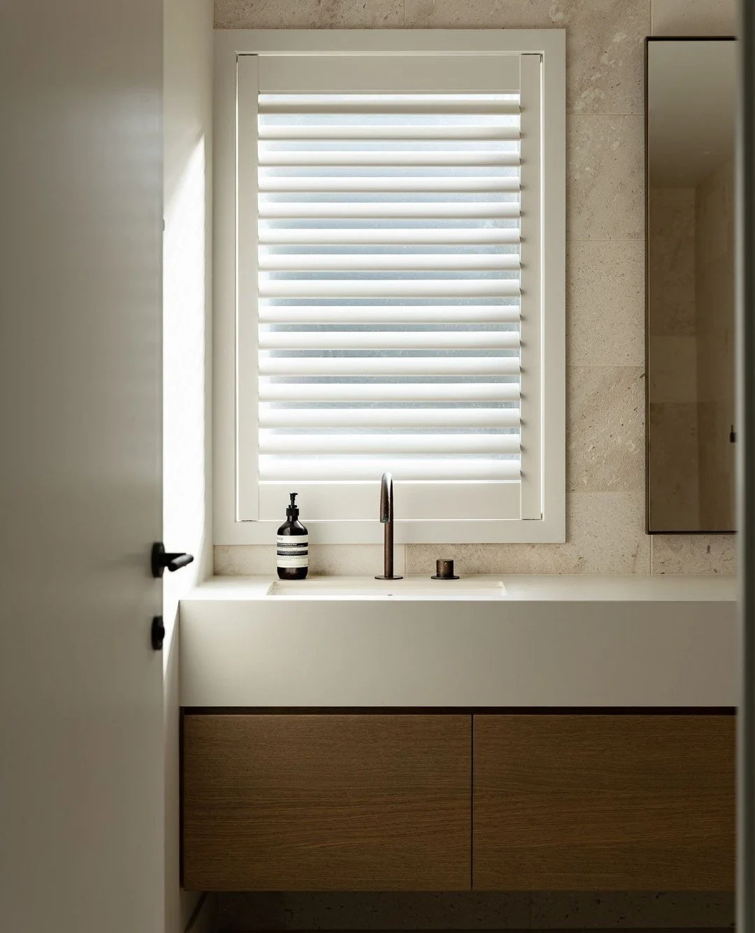Soft late afternoon light filtering through shutters settles gently across the space.⁠
Textural travertine and mid-toned timber layer in warmth and quiet depth.⁠
A generous, understated vanity anchors the room with effortless elegance.⁠
⁠
Nothing is 