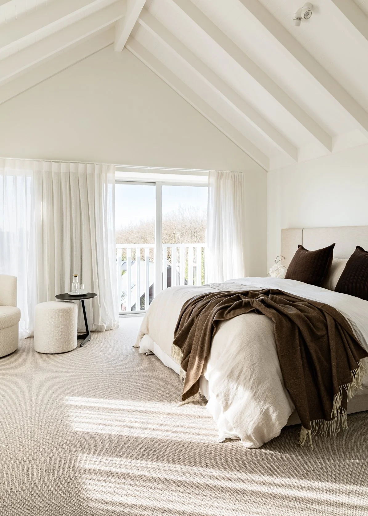 A dreamy master bedroom with gabled ceilings, white walls and sheer drapes. Flooring Xtra carpet in a soft sand / taupe loop pile adds softness and texture to the space.
