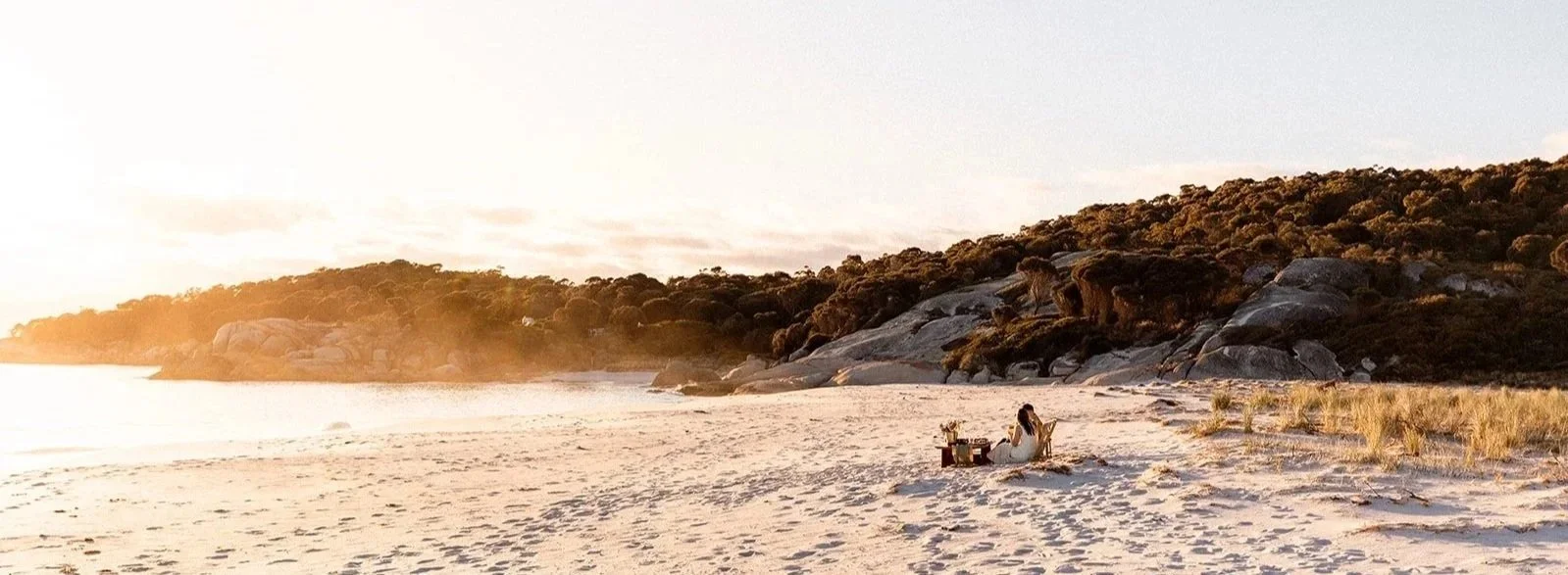 A woman and a man sitting on a beach at sunrise in Tasmania.