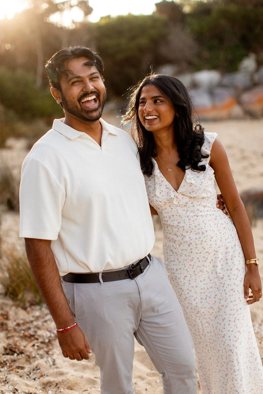 A smiling man and woman standing on a beach during sunset, enjoying each other's company.