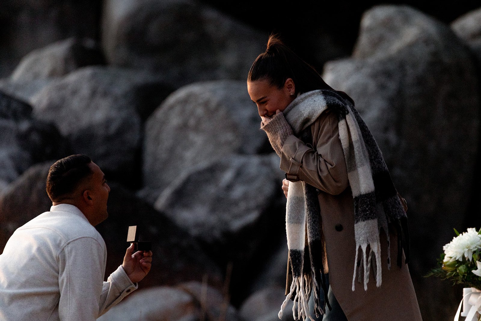 A man proposing to a woman by offering a ring, with rocks in the background.