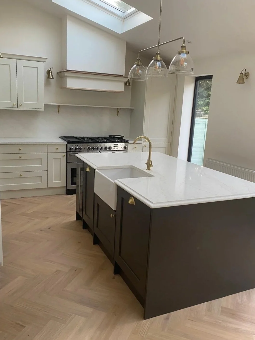 Modern kitchen with gray cabinets, a large white island with a sink, hanging pendant lights, a stainless steel refrigerator, stove, and baked goods on the island.