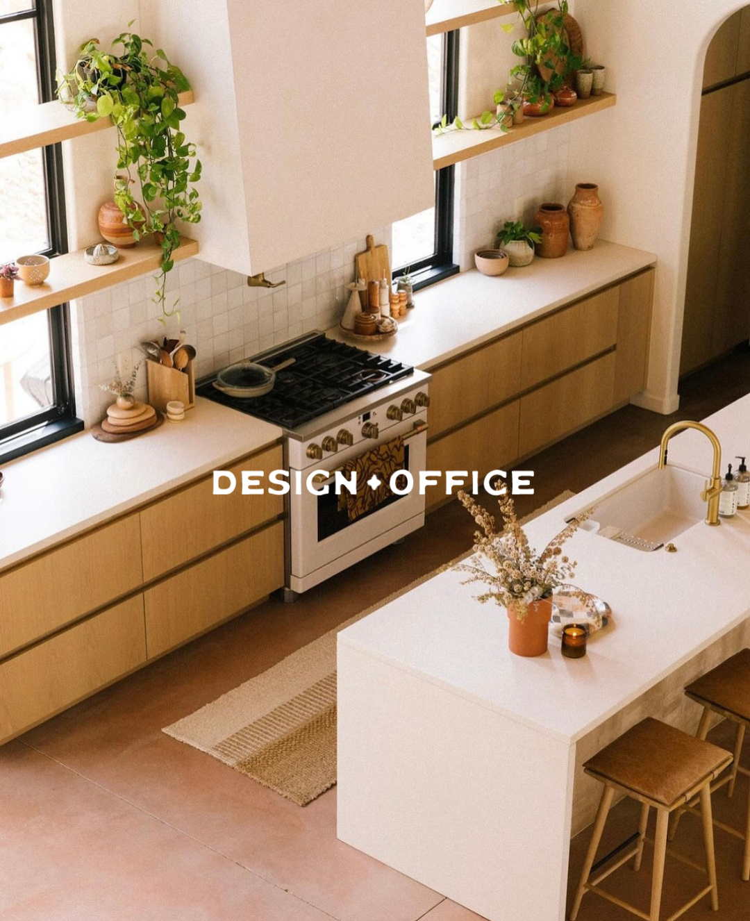 A modern kitchen with wooden cabinets, a white countertop island with two brown bar stools, a sink with a gold faucet, and potted plants on windowsills and shelves.