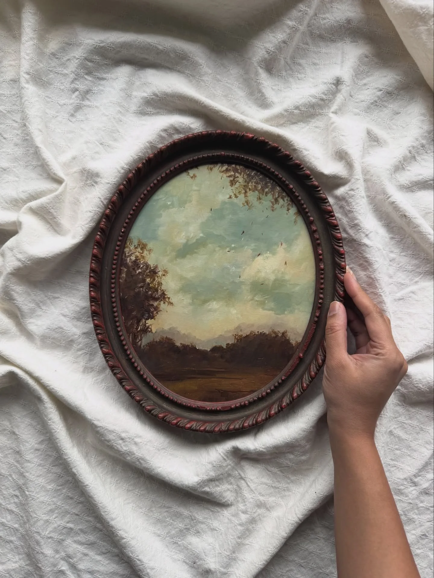 This original oil painting was created for those who want their home to feel considered, layered and deeply personal.

An oval landscape in a vintage-inspired frame, painted in soft sky blues and earthy browns, it captures a quiet countryside moment,