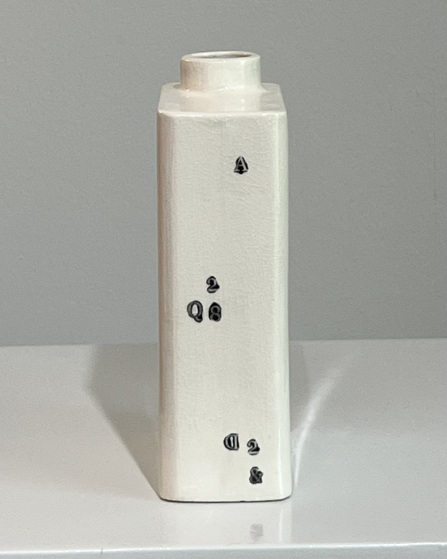 Opposite side view of a white porcelain milk carton with fragmented black typography.