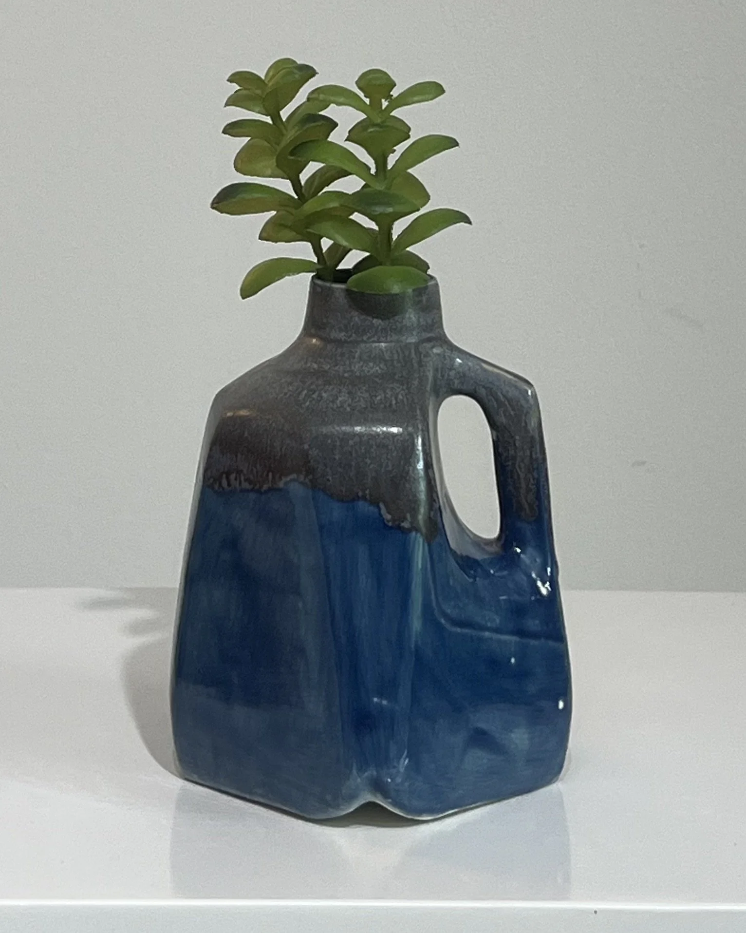 Handmade porcelain milk jug with layered cobalt blue and smoky gray glazes displayed with a small green plant.