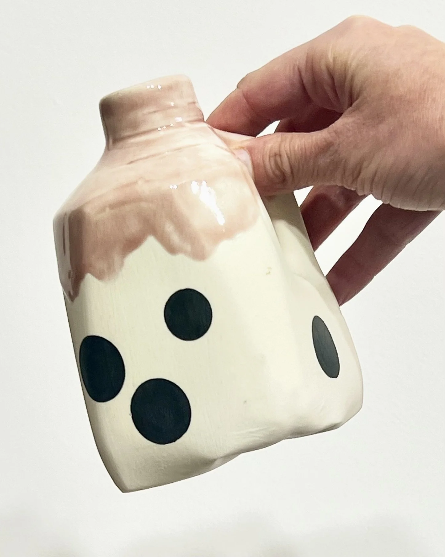 Hand holding handmade polka dot porcelain milk jug No. 26.149 to demonstrate its compact size, curved handle, and black-and-white spotted decoration.