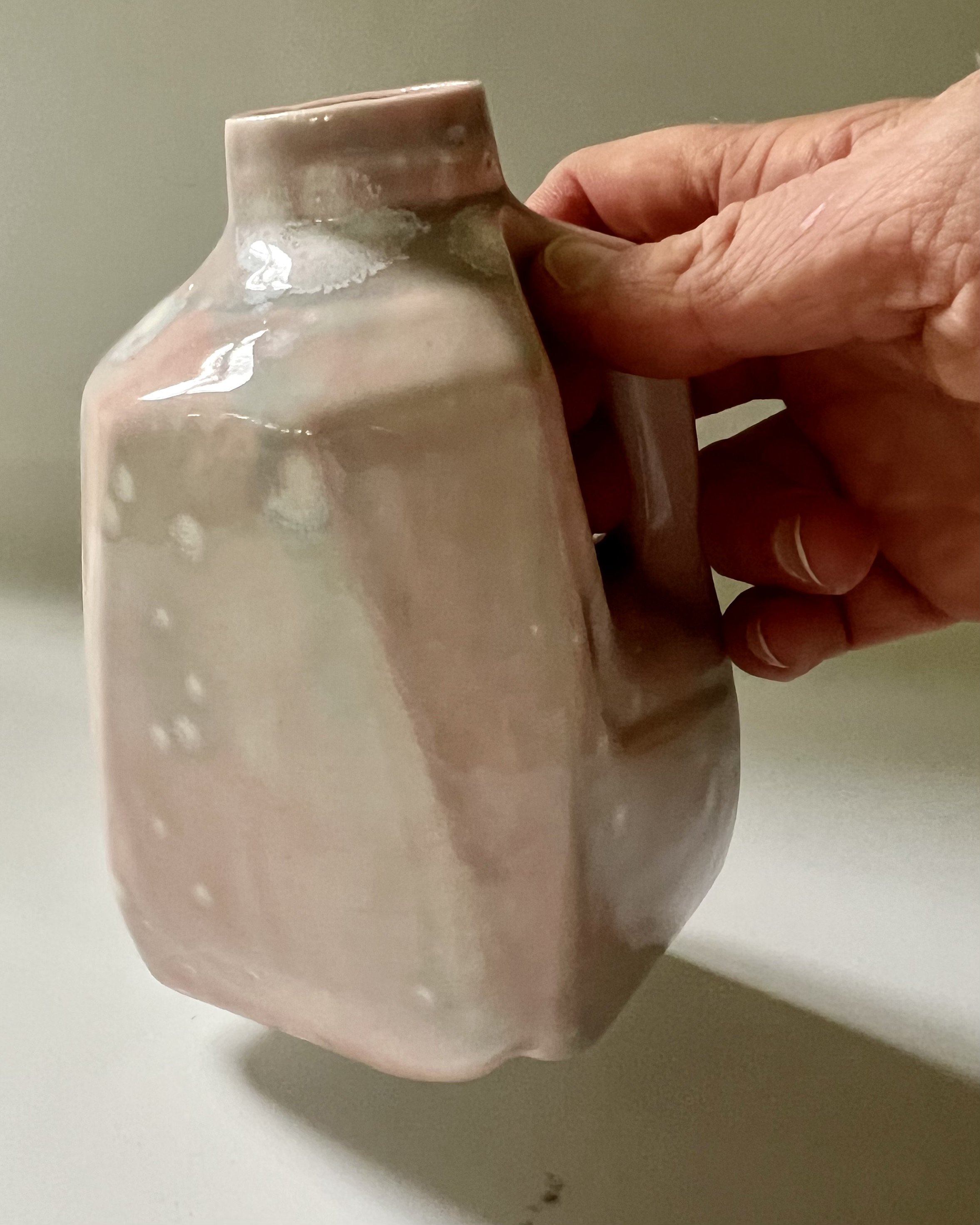 Hand holding porcelain milk jug to show scale and handcrafted design.